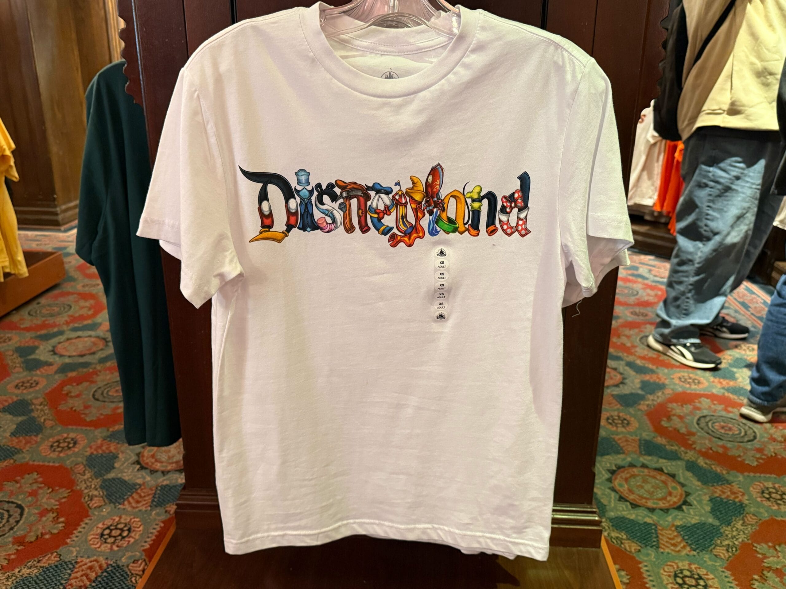 White t-shirt with “Disneyland” in colorful letters on a rack, among Disneyland park shirts