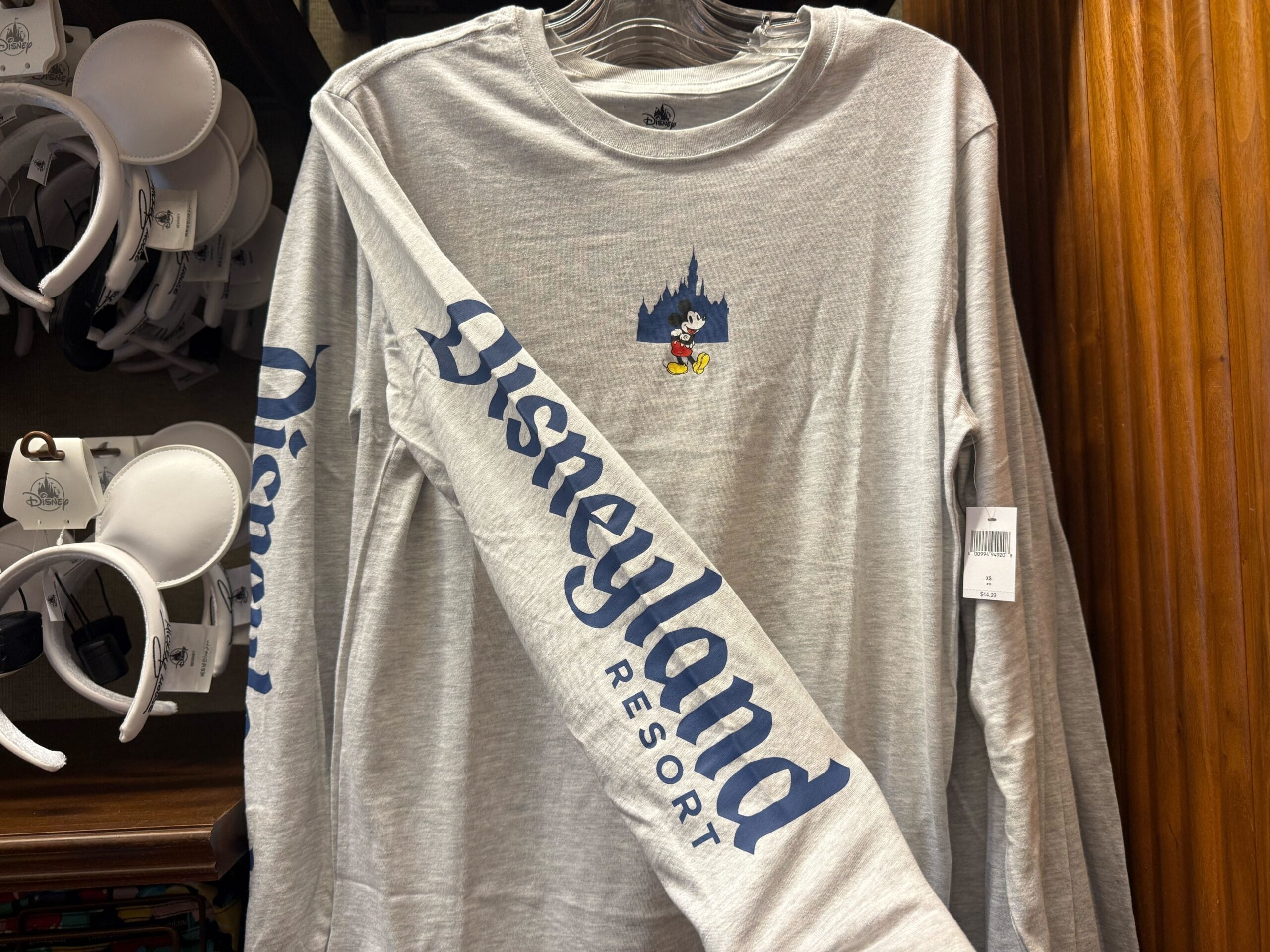 Gray Disneyland Resort long-sleeve shirt with Mickey Mouse, blue sleeve text, and shirts nearby