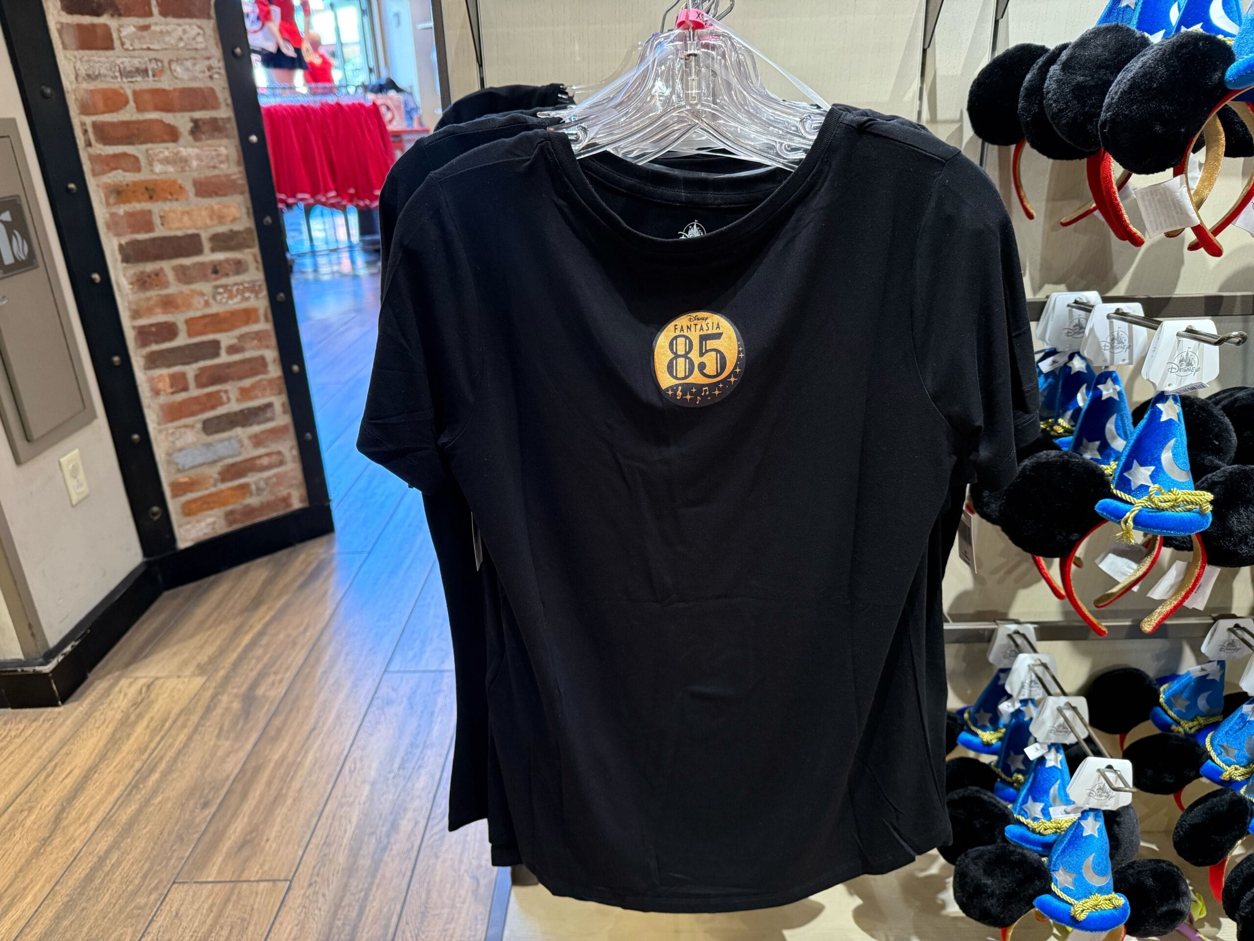 Black Disneyland tee with a bold "85 Years of Magic" badge, hanging in a park shop