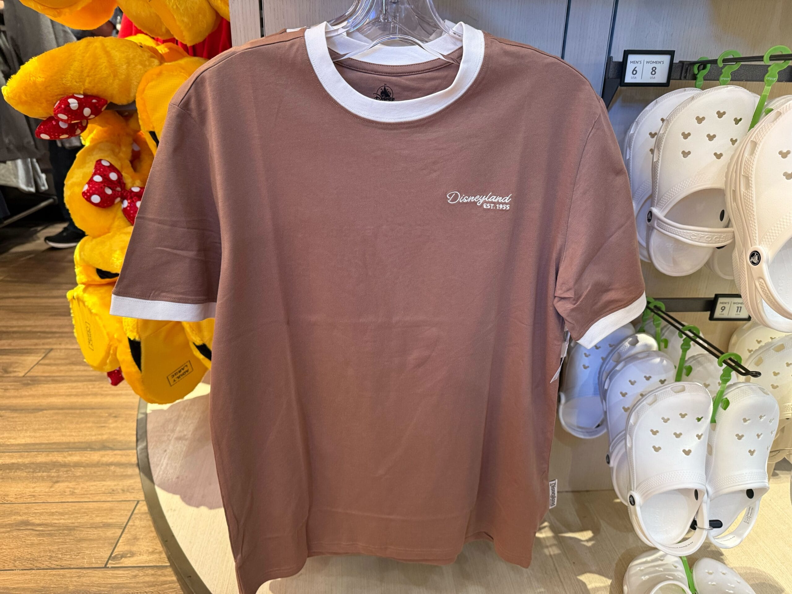 Light brown Disneyland shirt with white collar and cuffs on a hanger, next to white sandals and plush toys
