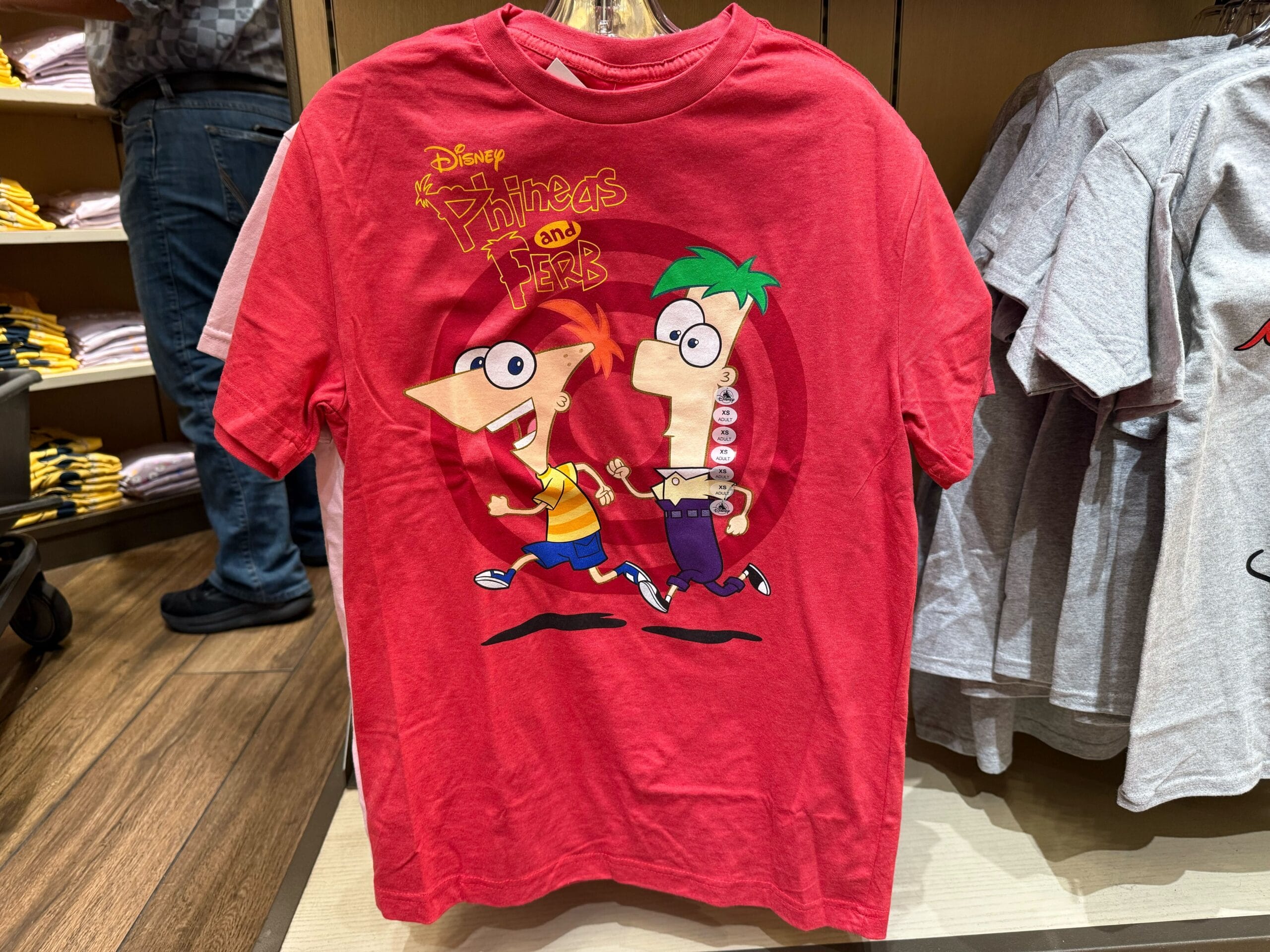 Red T-shirt featuring Phineas and Ferb running, displayed with other new Disneyland shirts