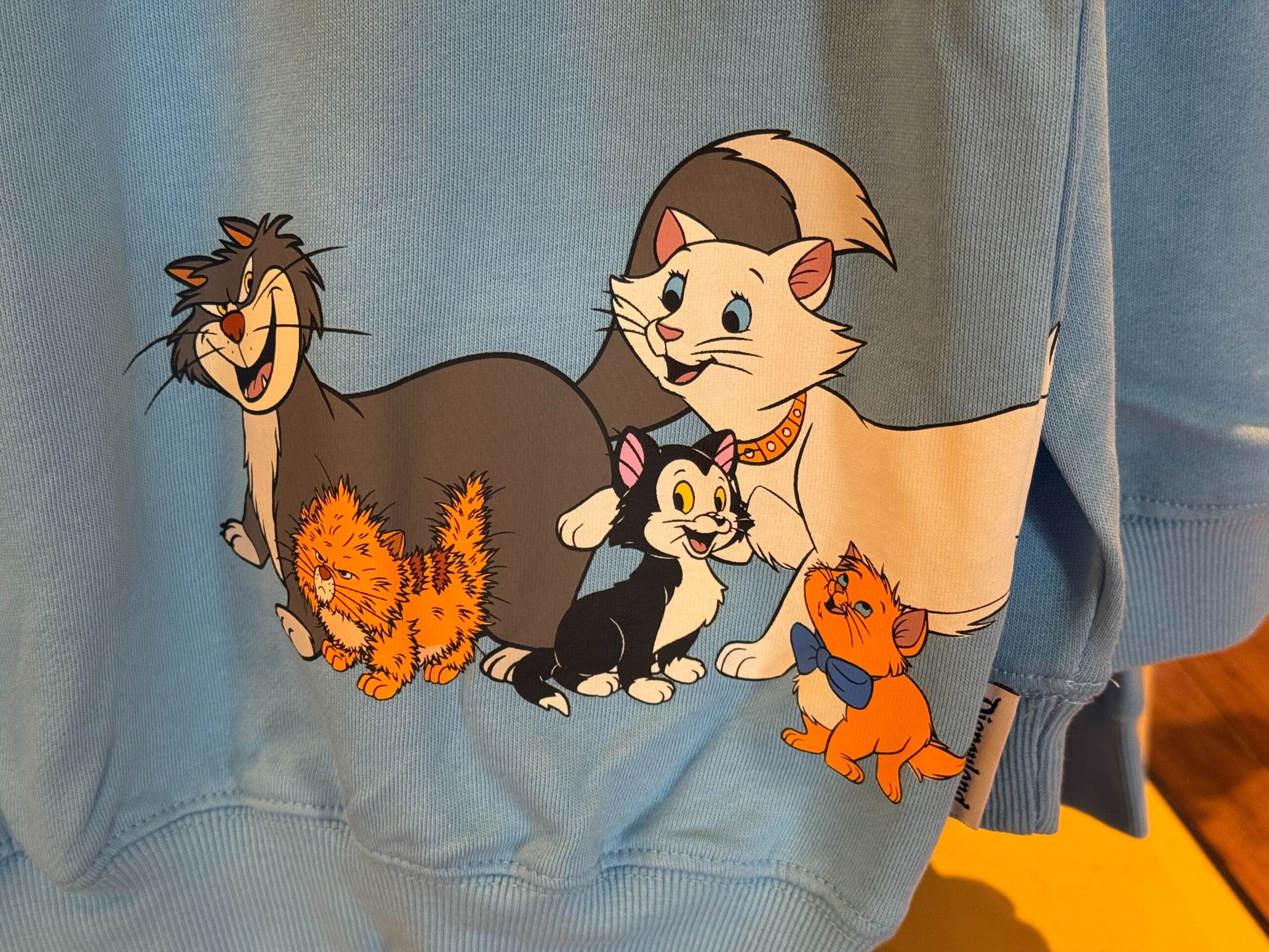 Cartoon cats in bright colors and playful poses cover a blue fabric, reminiscent of whimsical Disney merchandise designs.