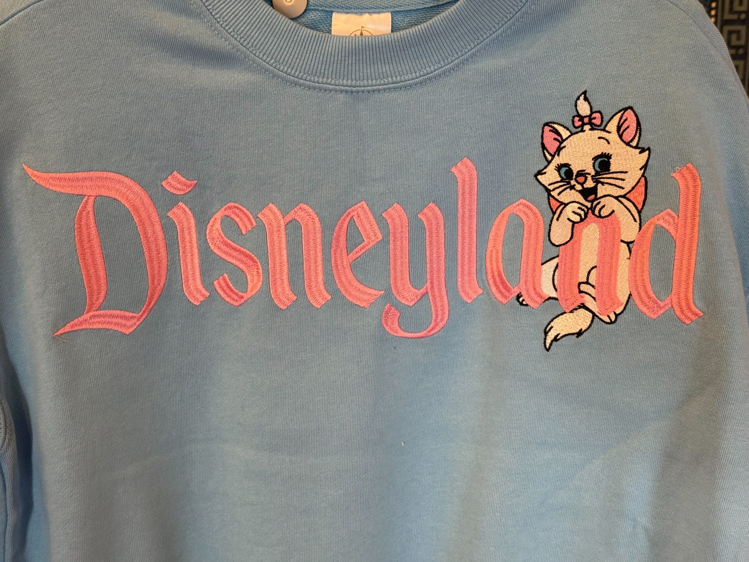 Light blue Disneyland sweatshirt with pink lettering and an adorable white cartoon kitten, perfect for Disney park fans worldwide.