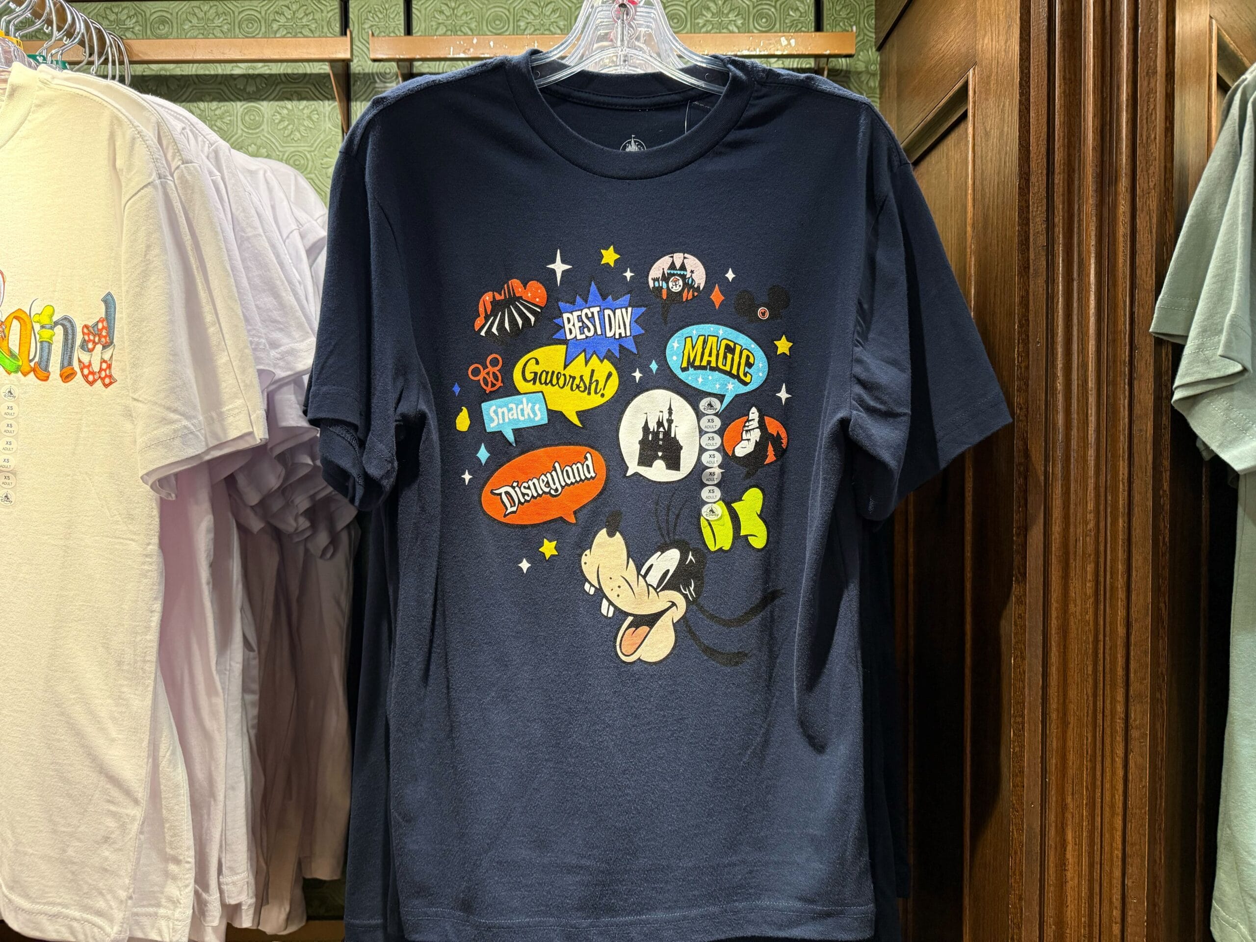 Navy blue Disneyland shirt featuring Goofy and colorful park icons; design references classic Disneyland style