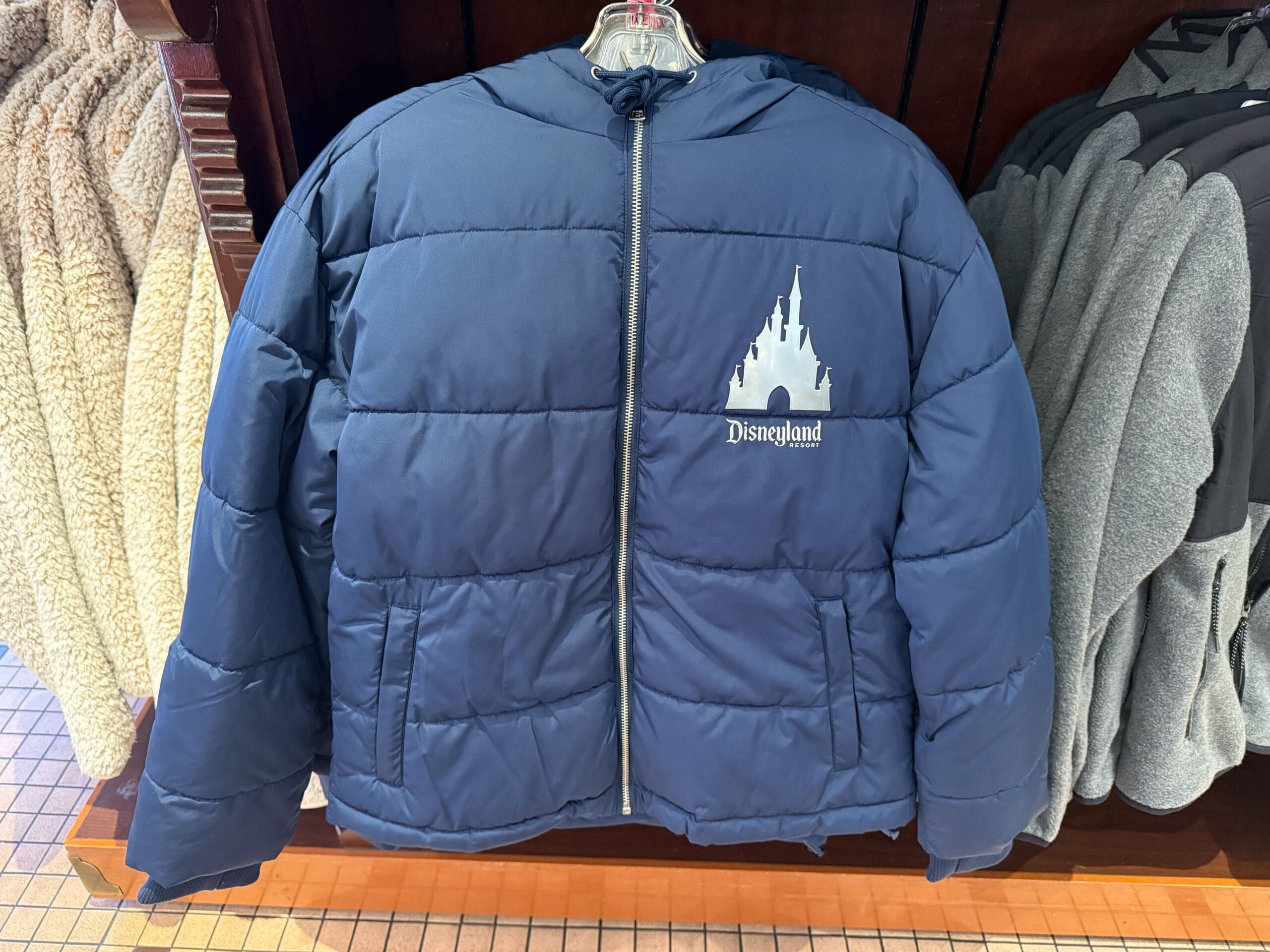 Navy blue puffer jacket featuring a white Disneyland castle logo resembling Sleeping Beauty Castle, ideal for Disney park fans.