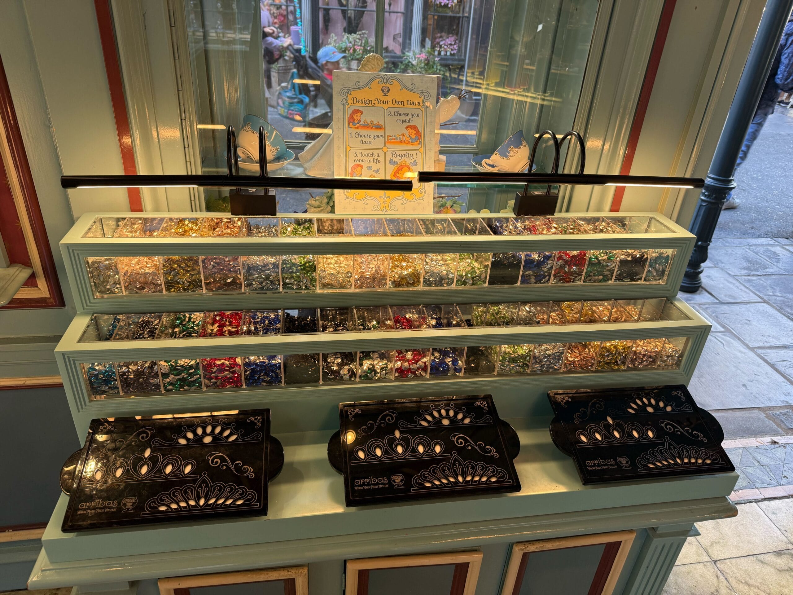 A jewelry display at a Disney park shop shows colorful beads, silver charms, and Halloween tiaras for customizing