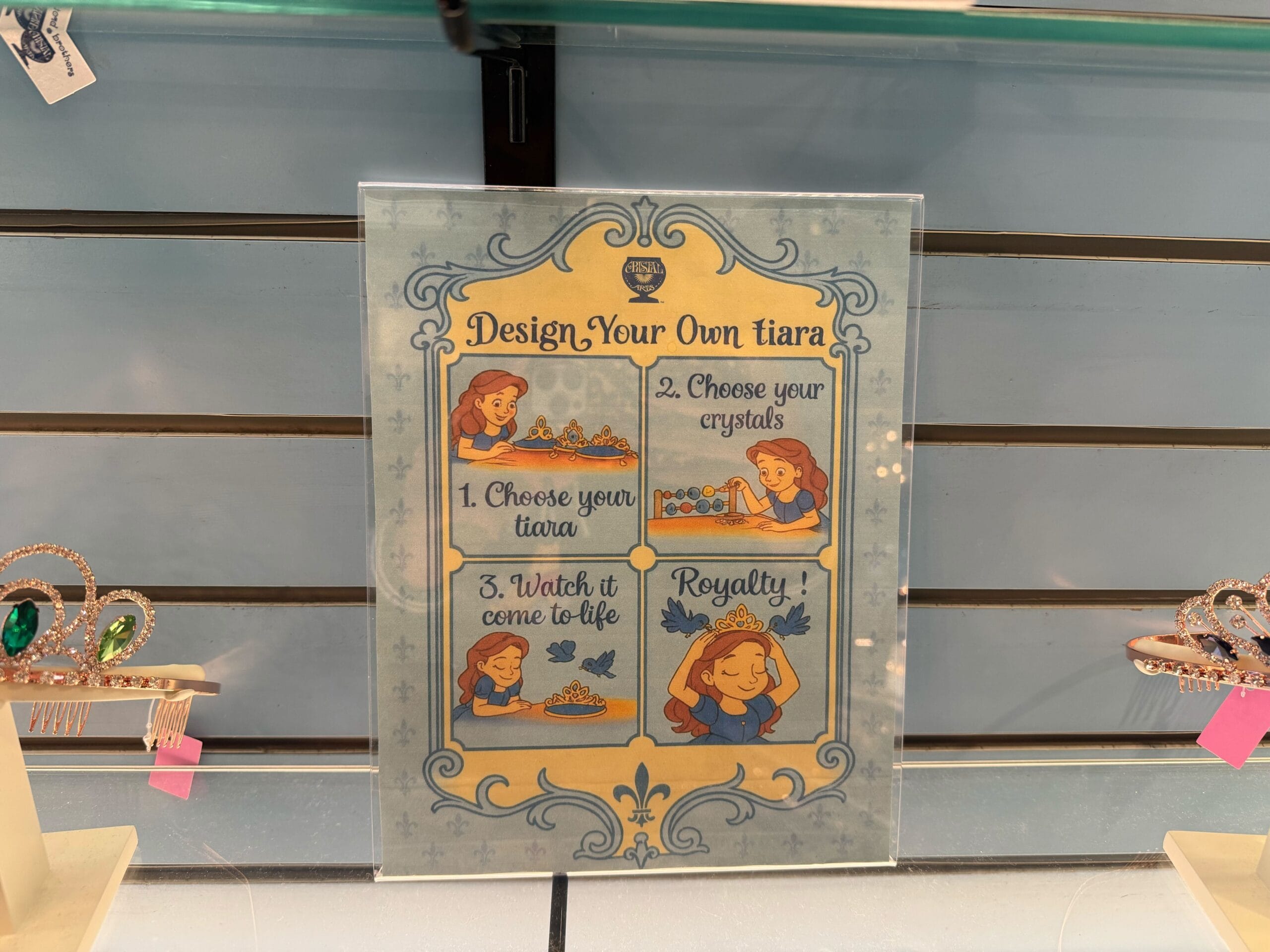 Instruction sign with illustrated steps for designing Halloween Tiaras, tiaras shown on sides; Disney Parks-inspired details visible.