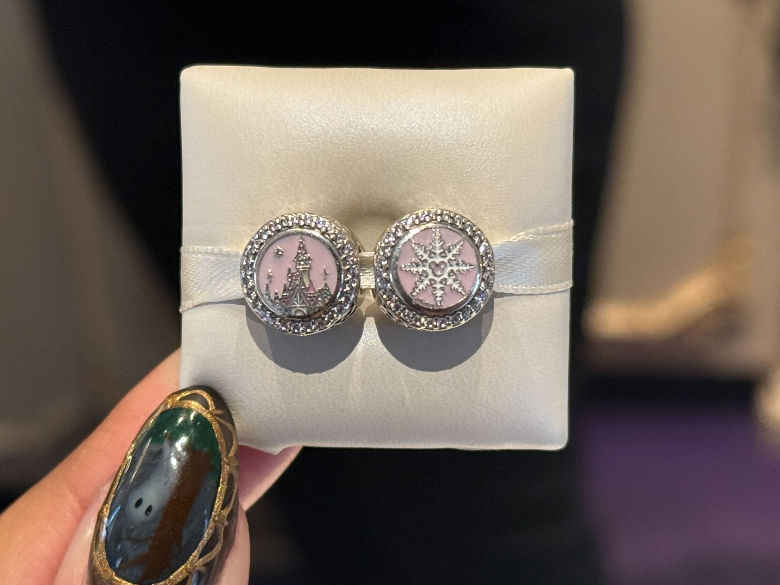 A hand holds earrings on a cushion—one with a castle resembling Sleeping Beauty Castle, the other a star—Disney park fan favorites.