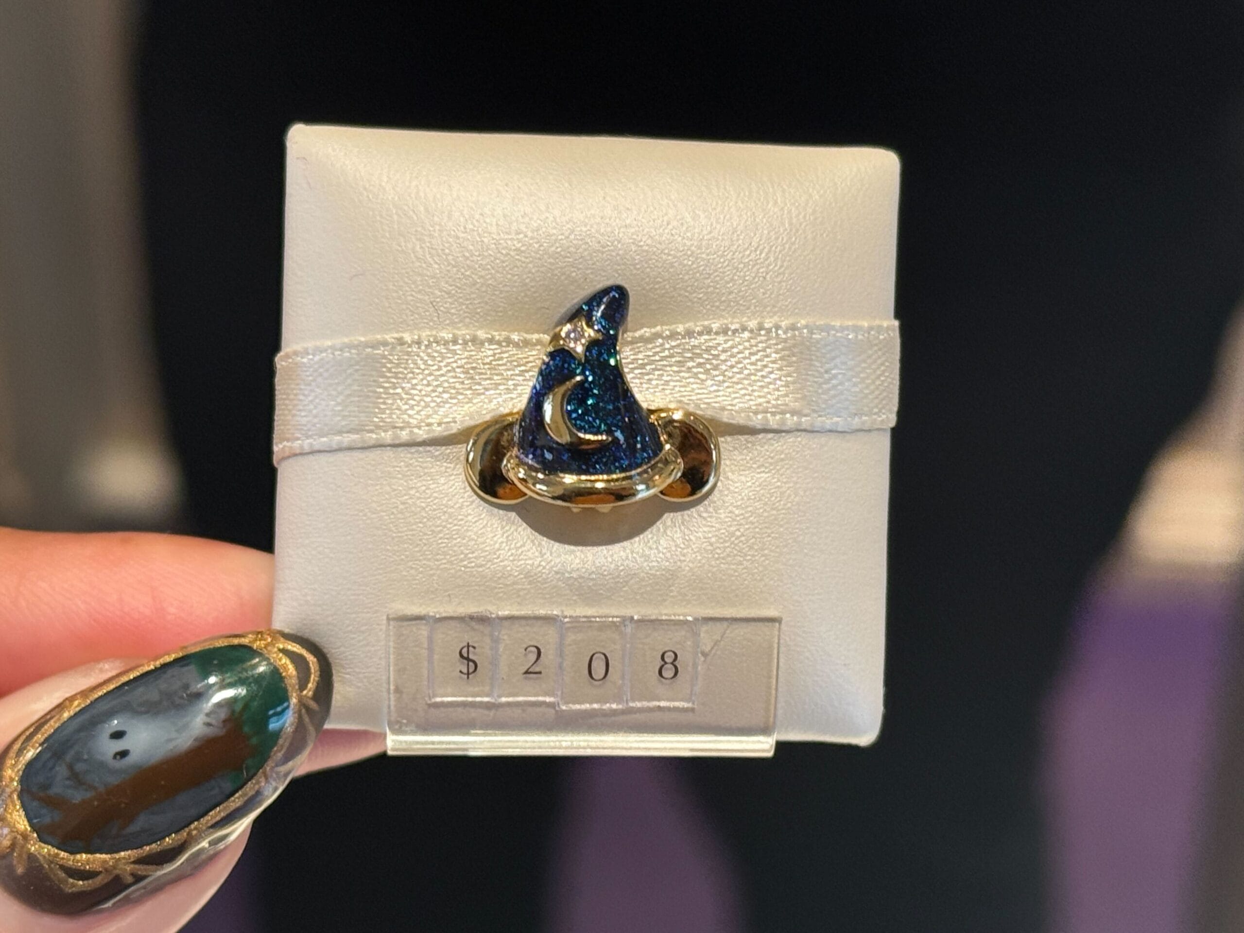 A hand displays a blue Sorcerer Mickey hat ring, Pandora-style, for $208—just like magic found in Walt Disney Park shops.