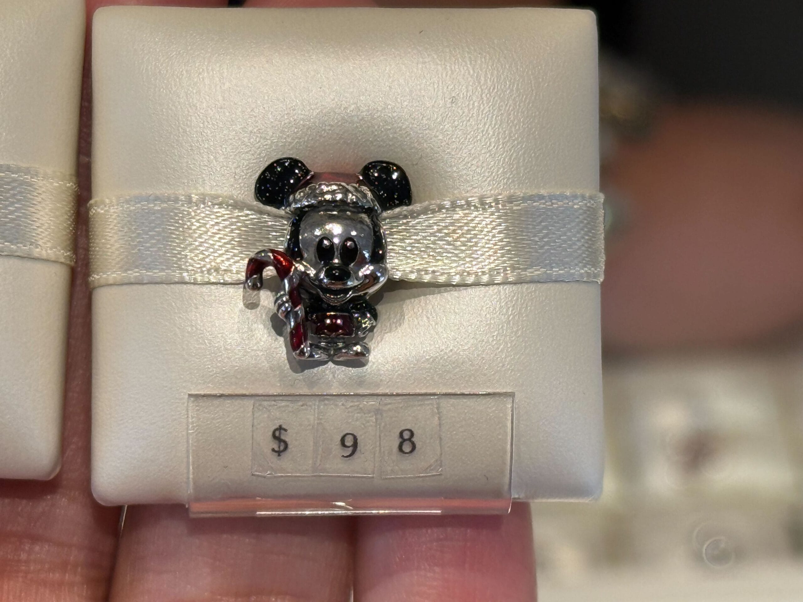 A Disneyland Pandora Charm features Mickey Mouse with a candy cane on a cushion, $98 price tag, fitting the park’s festive magic.