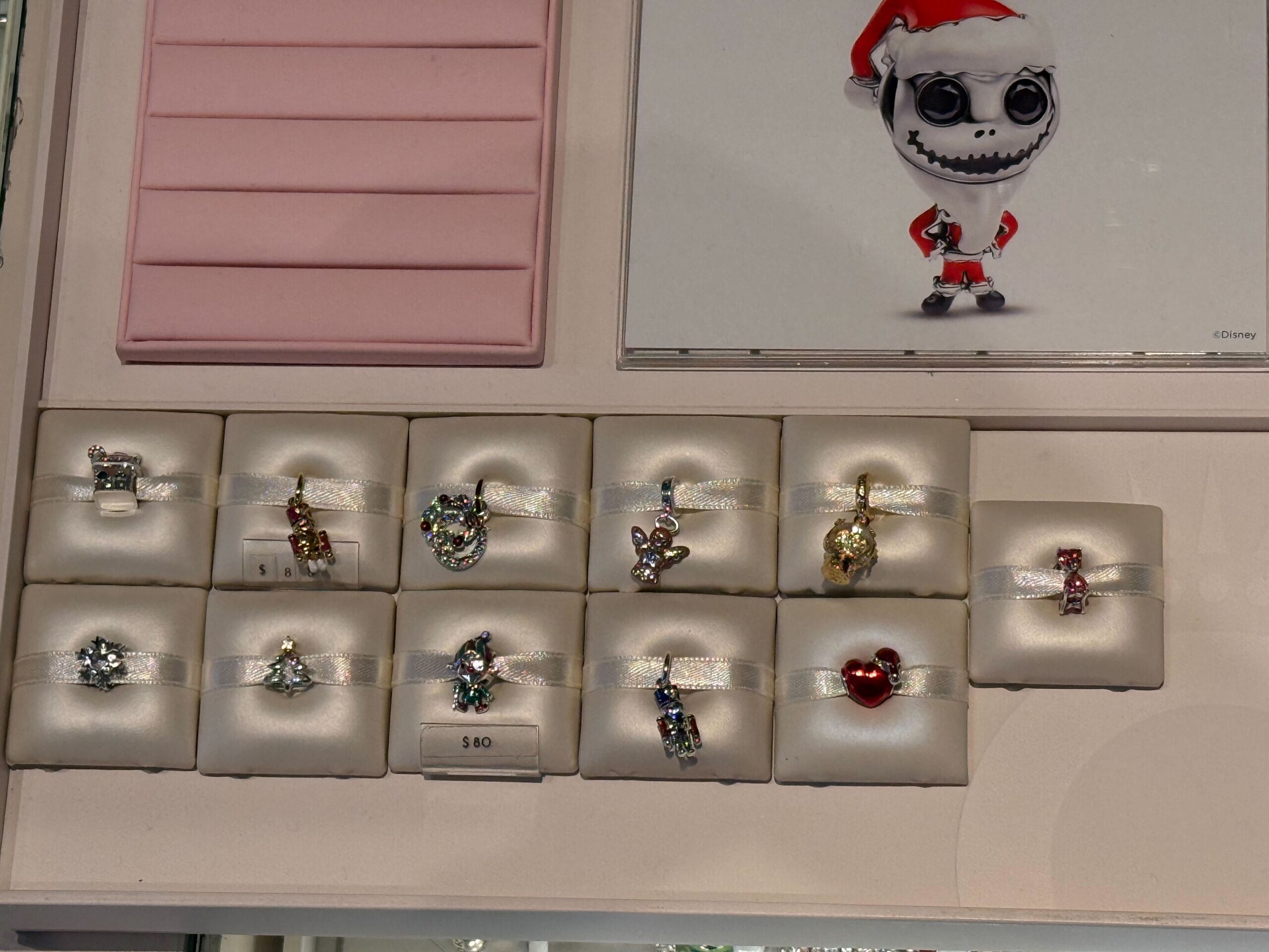 A display of ten holiday-themed Pandora Charms in a jewelry case, $60 tag, reminiscent of Main Street shops at Disney Parks.