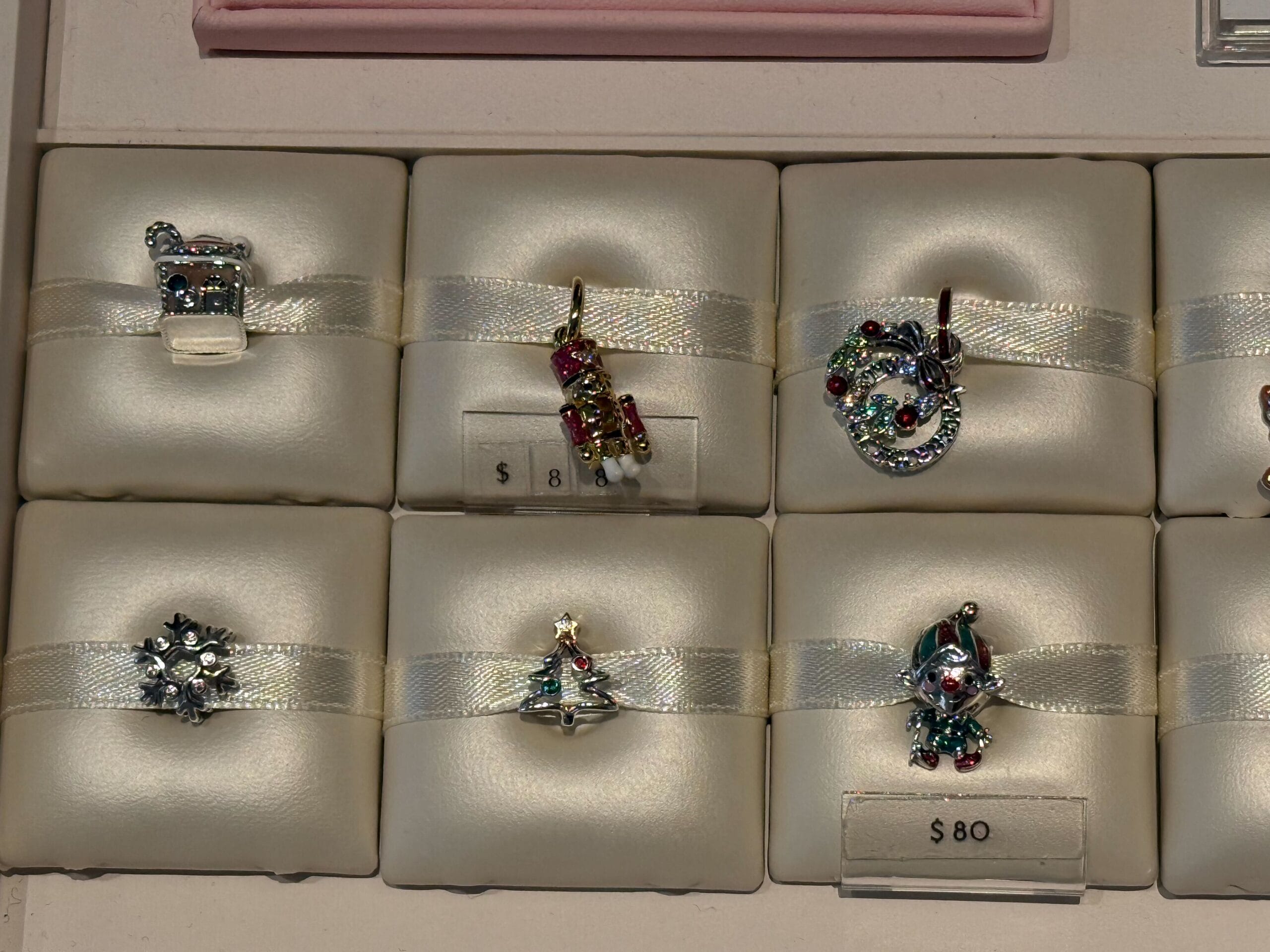 Six Christmas Pandora Charms—wreath, tree, gifts, and snowman—on padded cream holders, reminiscent of Disney park holiday magic.