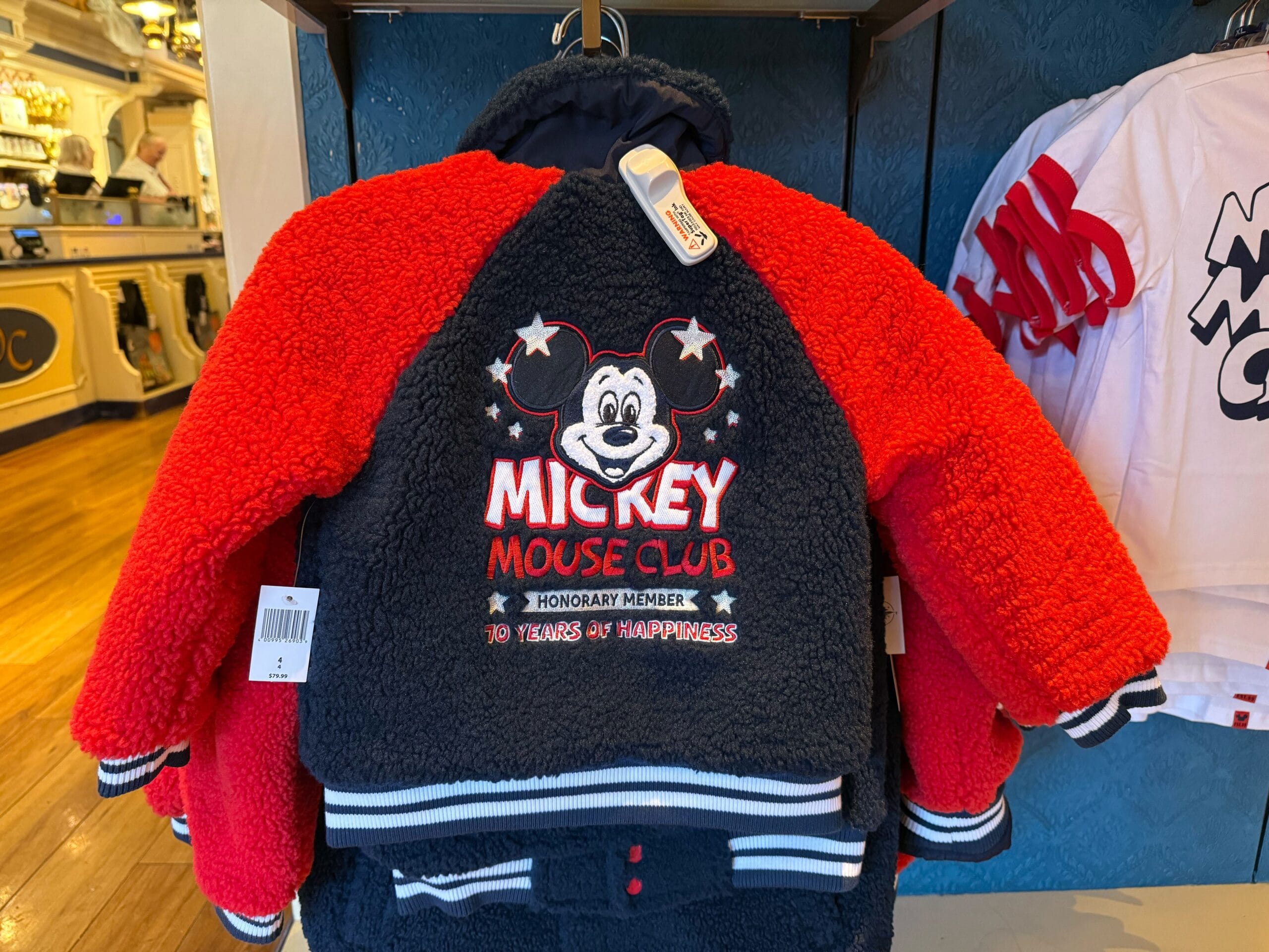 Red and navy 70th Anniversary Mickey Mouse Club jacket for kids, displayed on a rack in a store.