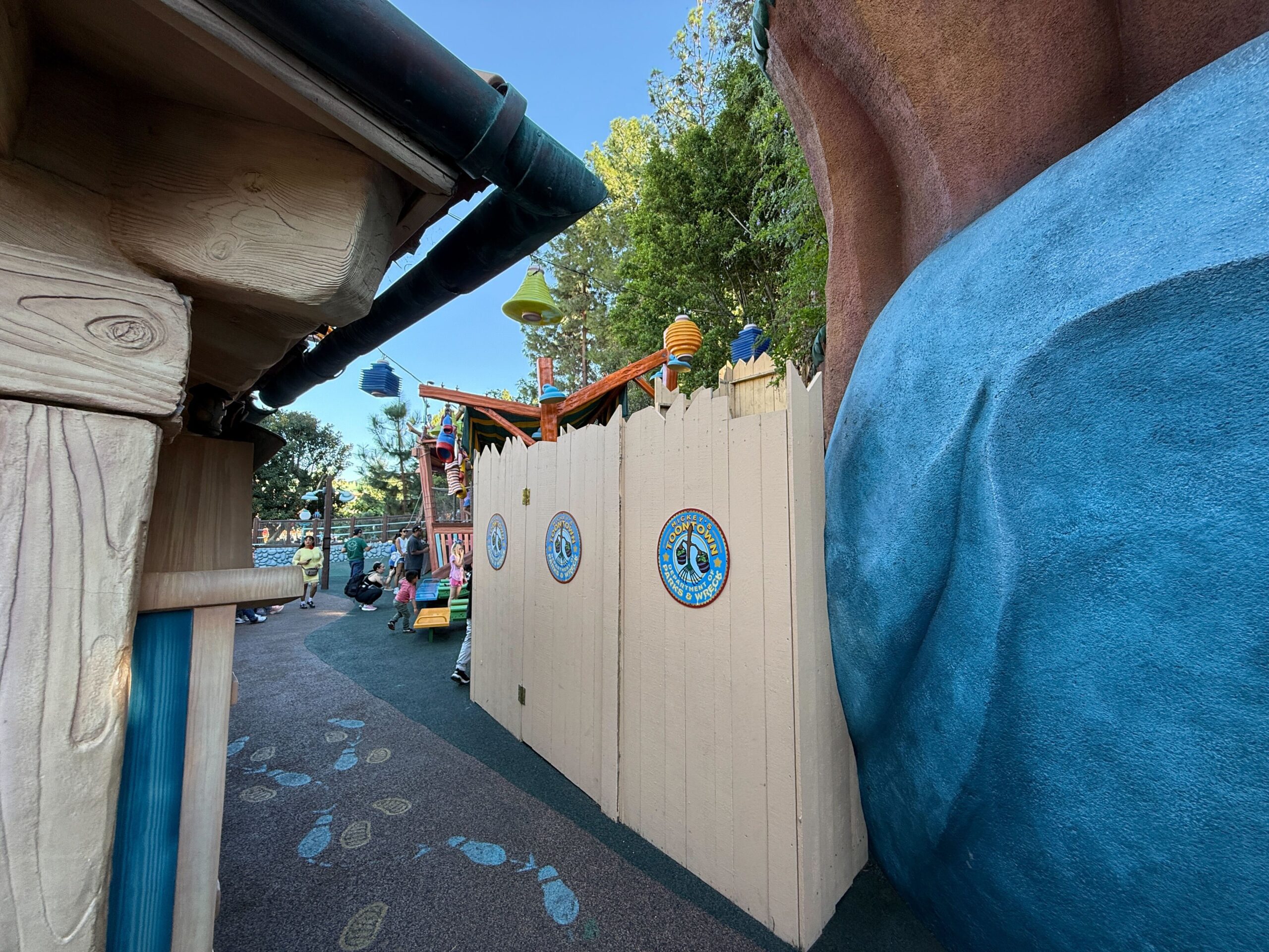 Tan construction walls with playful signs block a walkway in Disneyland’s Mickey’s Toontown, echoing the park’s whimsical style.