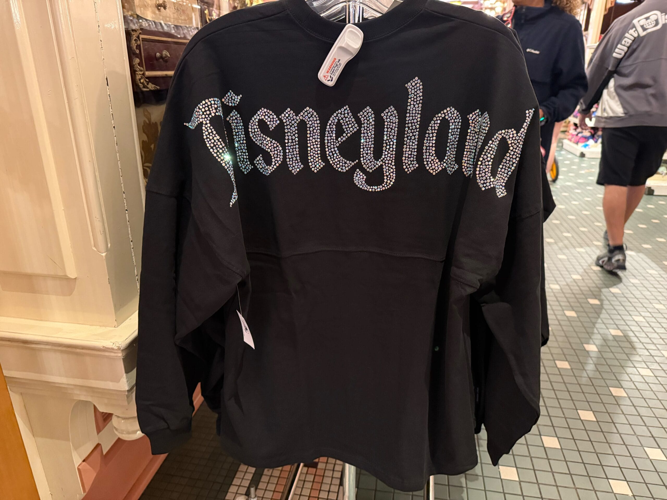 A black Disneyland Spirit Jersey with sparkling letters glitters on a store rack