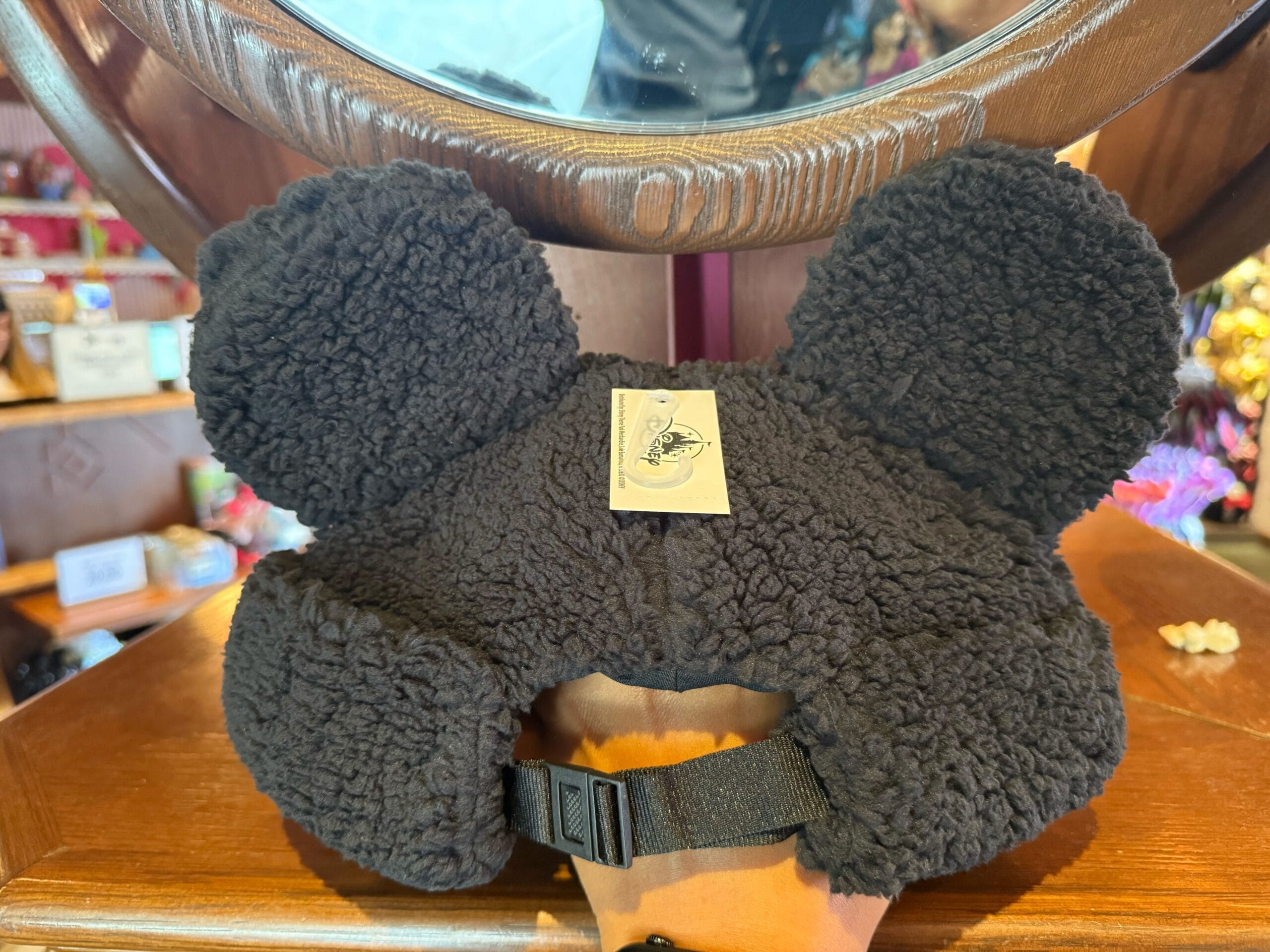 A fuzzy black Mickey Mouse hat with iconic round ears and a chin strap sits on a shelf, evoking classic Disney Park vibes.