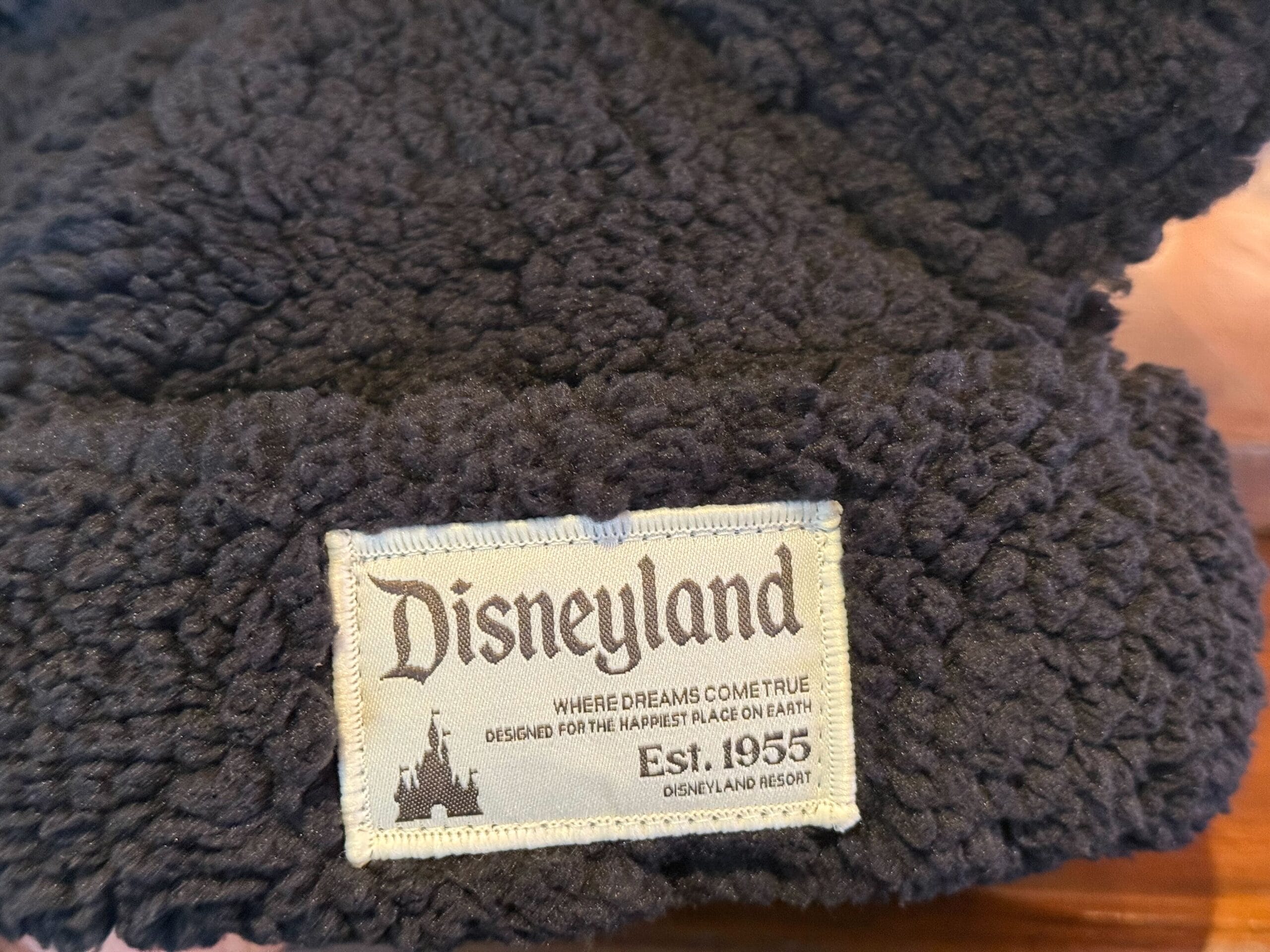 Close-up of a black fleece Sherpa Beanie with Disneyland label, "Est. 1955" and "Where dreams come true," echoing park heritage.