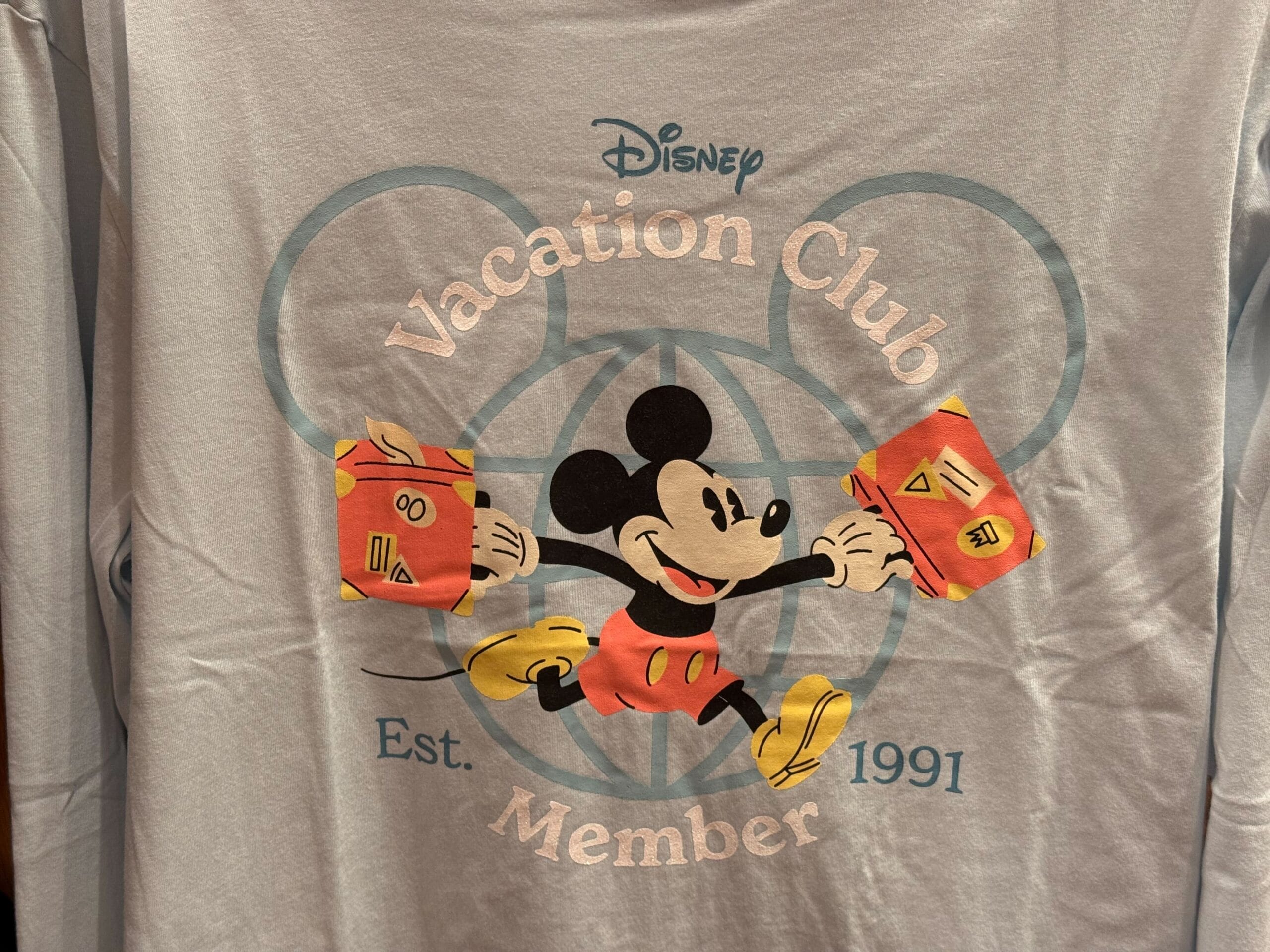 A shirt featuring Mickey Mouse with suitcases, classic Disney Vacation Club merch for members since 1991