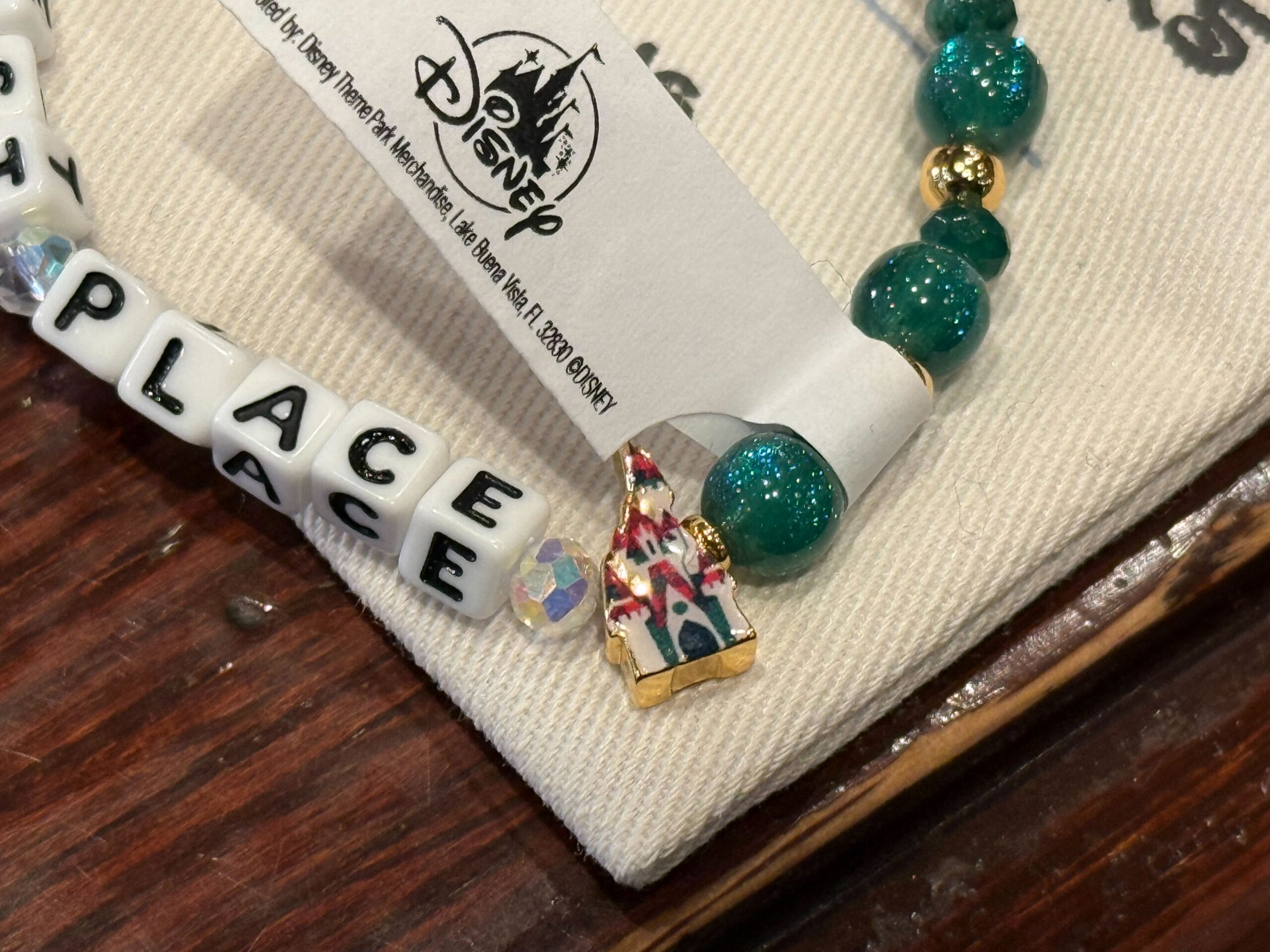 Beaded bracelet with "PLACE" beads and a castle charm resembling Sleeping Beauty Castle, part of Disneyland 2025 Christmas merch.