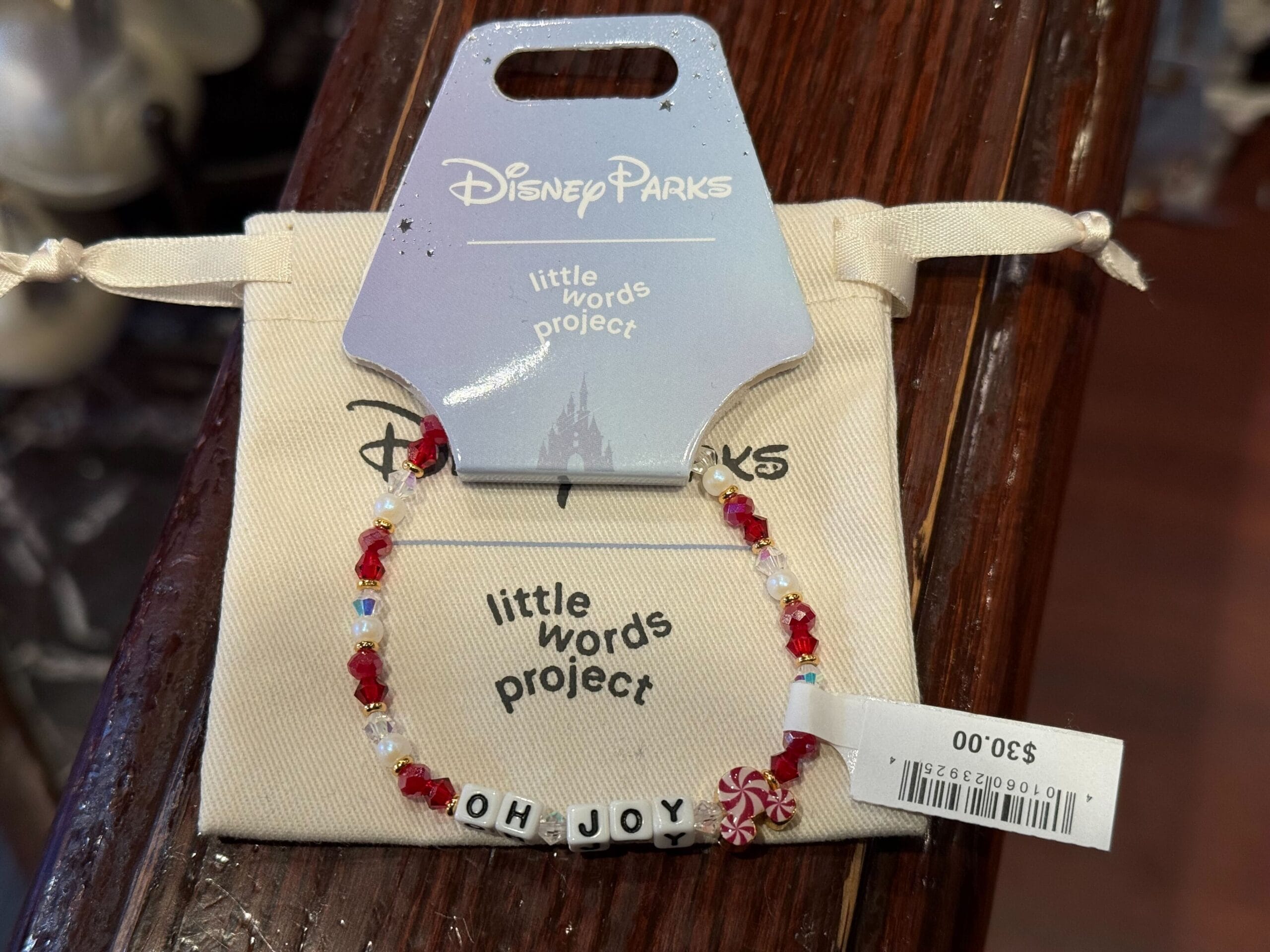 A festive "OH JOY" bracelet with red and white beads from Disneyland's 2025 holiday collection, priced at $30. No castle shown.