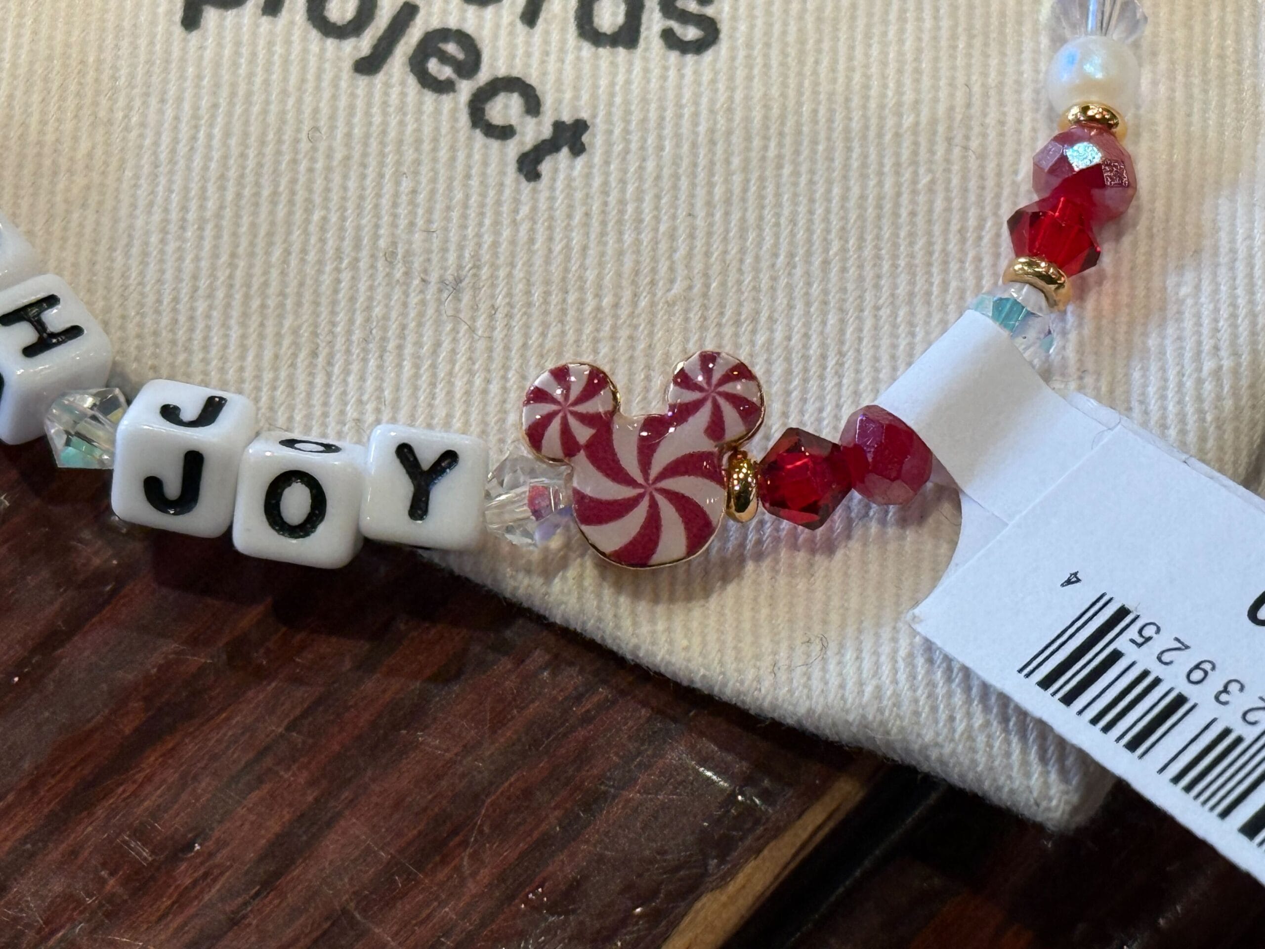 Disneyland Christmas bracelet with "JOY" beads and peppermint Mickey charm on a bag; festive 2025 park merch, no castle visible.