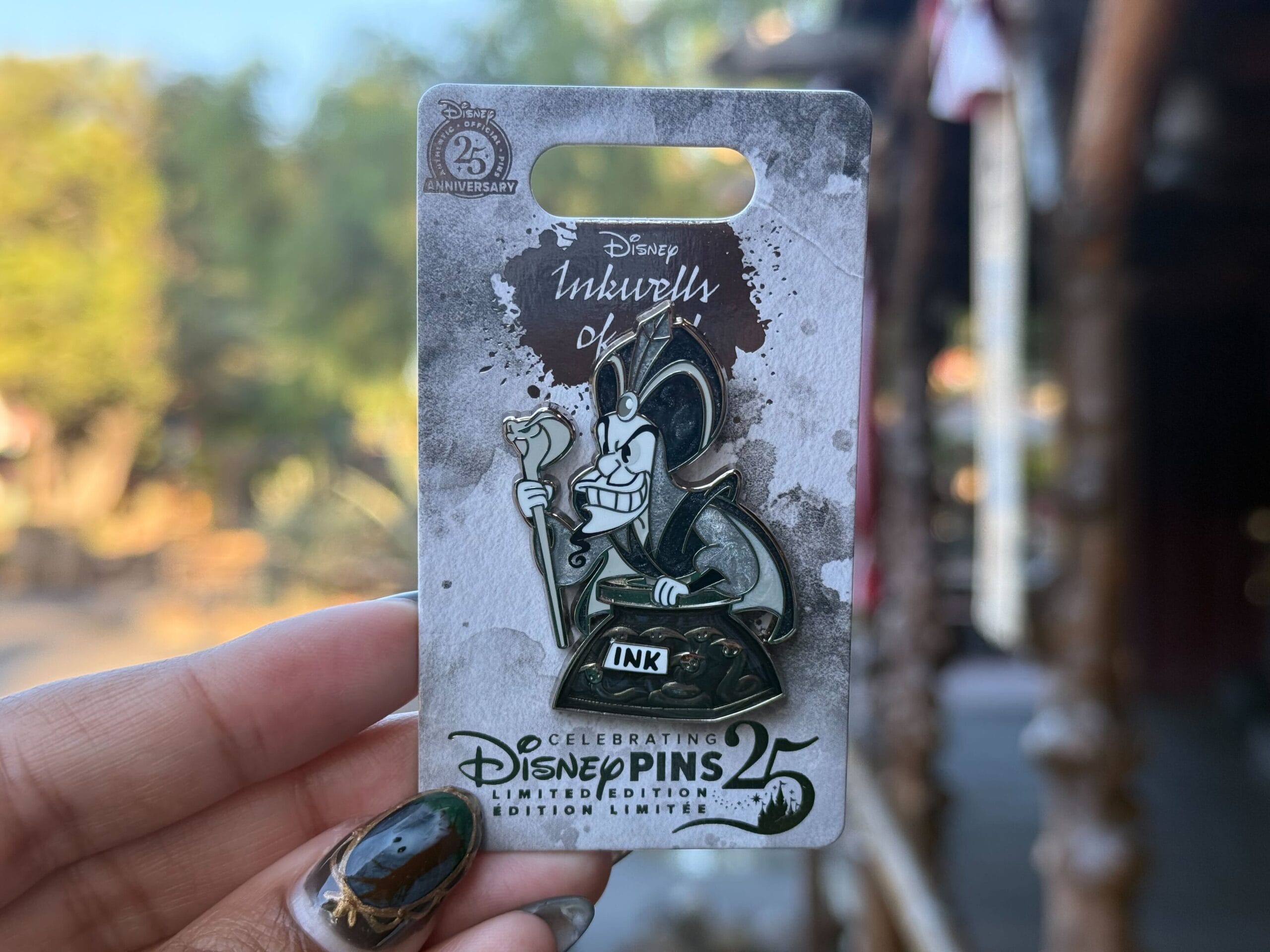 A hand displays a Jafar Inkwells of Evil pin on a Disney Pins 25th Anniversary card outside, no Disney castle in sight.