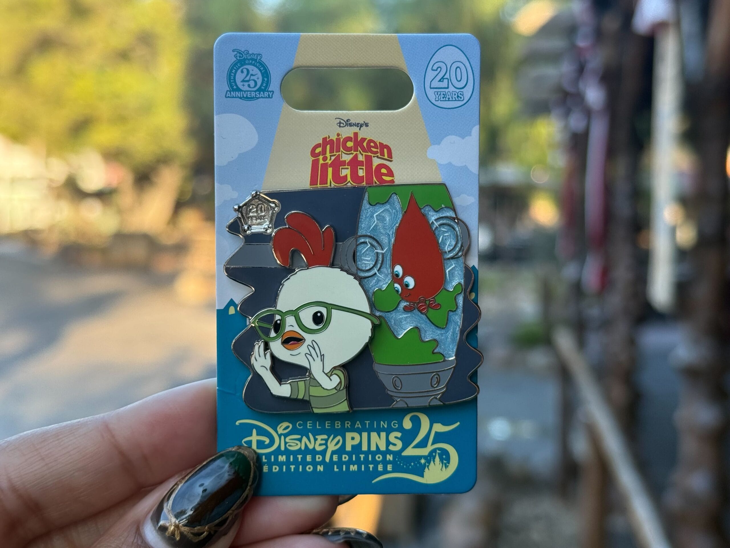 A hand displays a limited edition Disneyland Pin Tuesday pin with Chicken Little and a green alien, exclusive to Disney Parks.