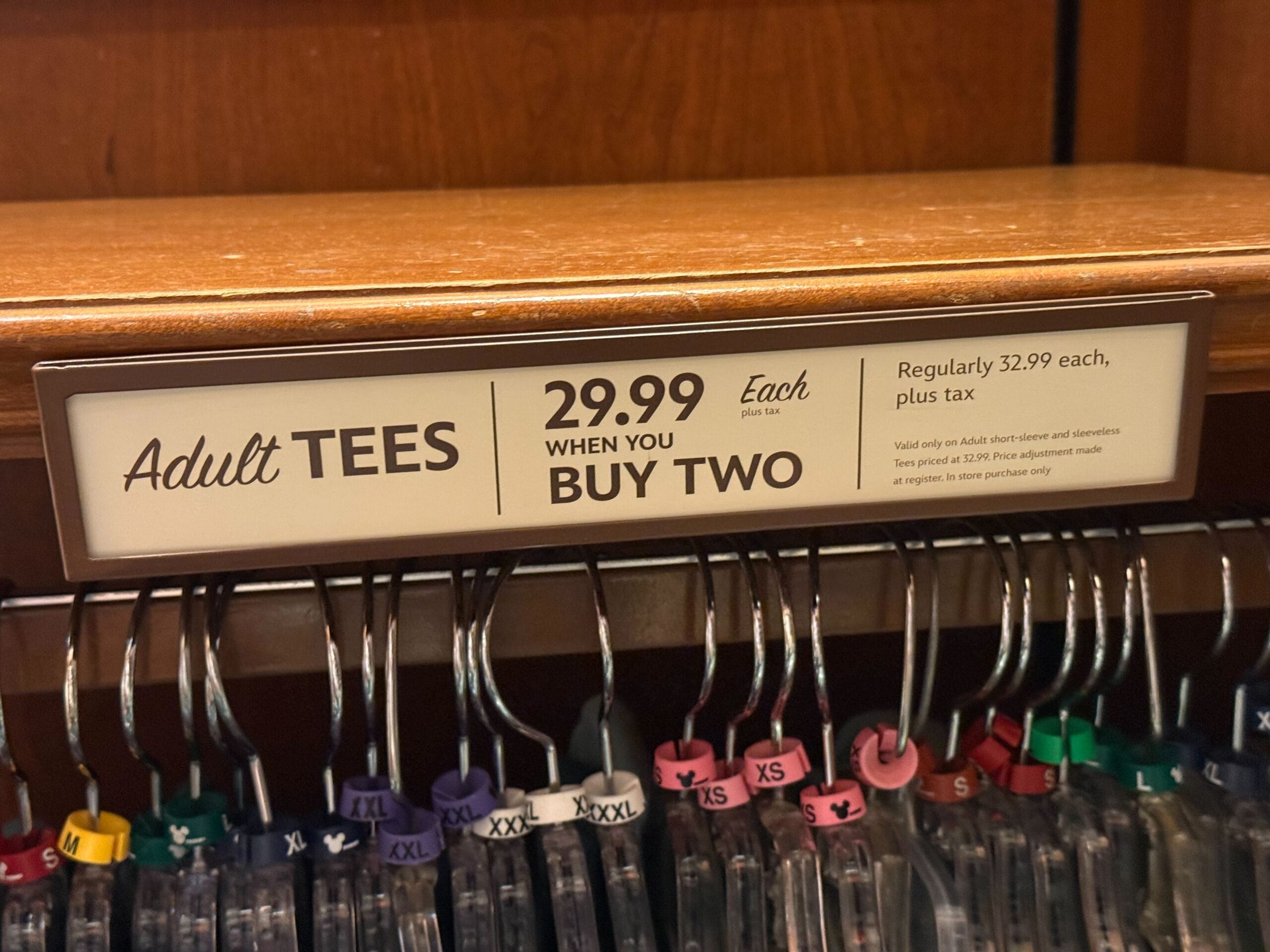 Disneyland store sign: Adult tees $29.99 each with purchase of two, reg. price $32.99 each, plus tax; no castle comparison shown.