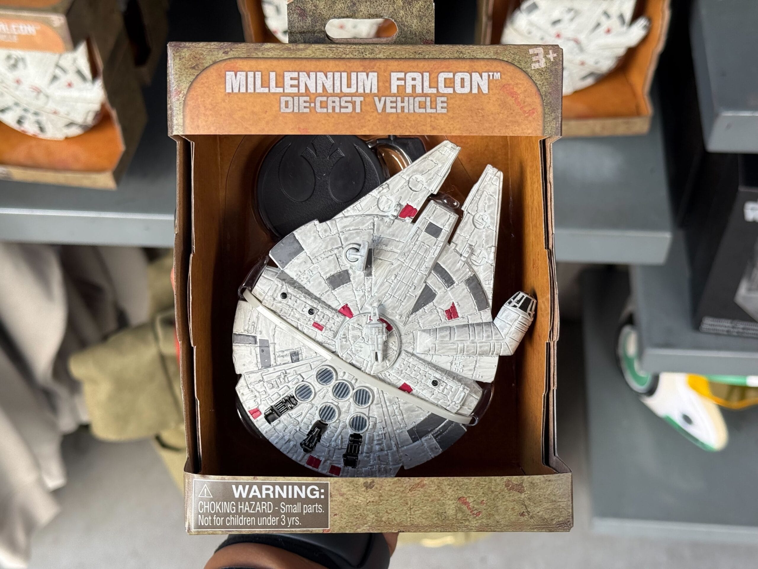 A die-cast Star Wars Millennium Falcon toy in Disney Parks-themed packaging, labeled 3+ with a choking hazard warning.