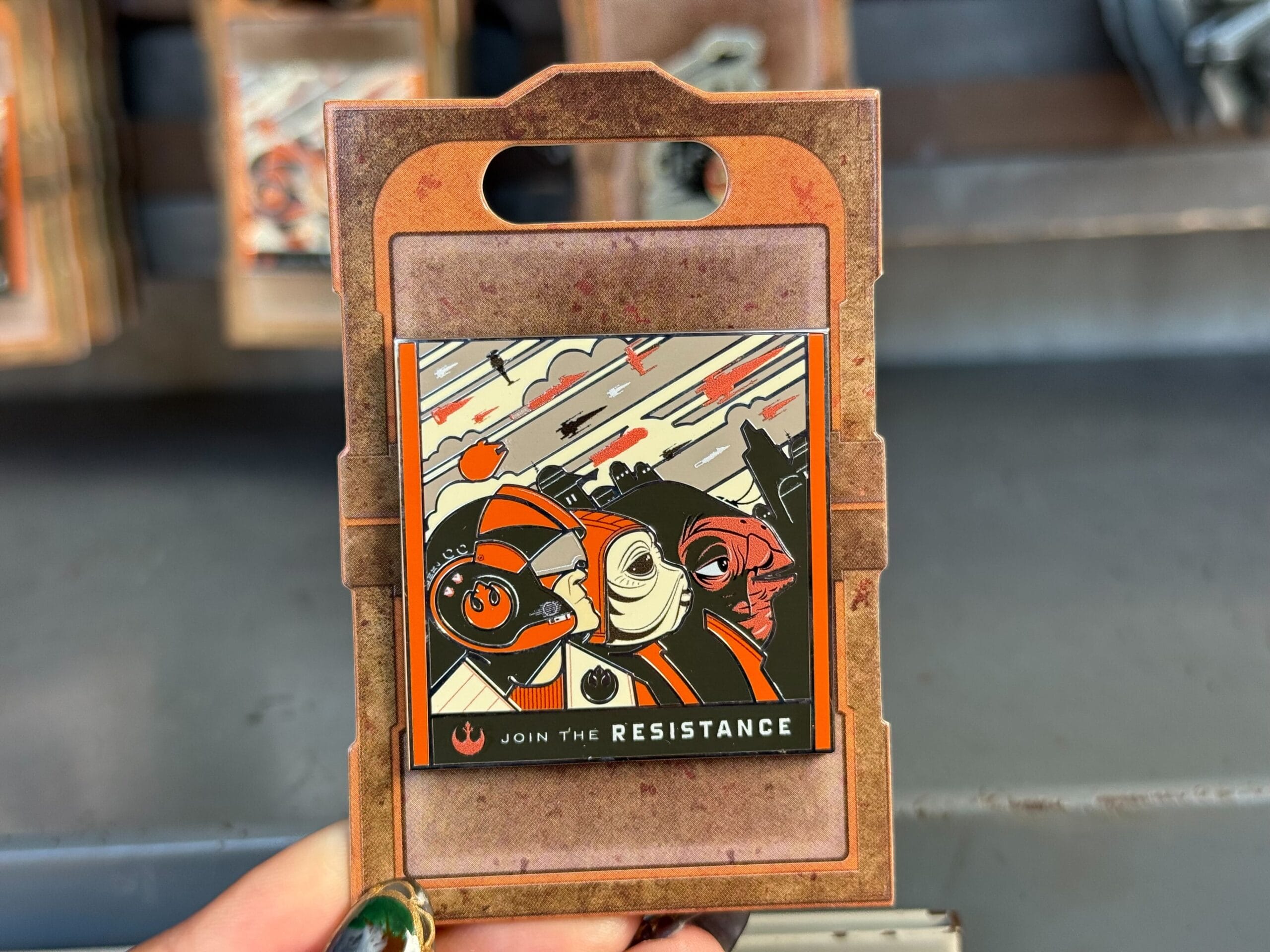 A hand holds a "Join the Resistance" Star Wars Galaxy's Edge pin featuring stylized ships and characters from Disney Parks.