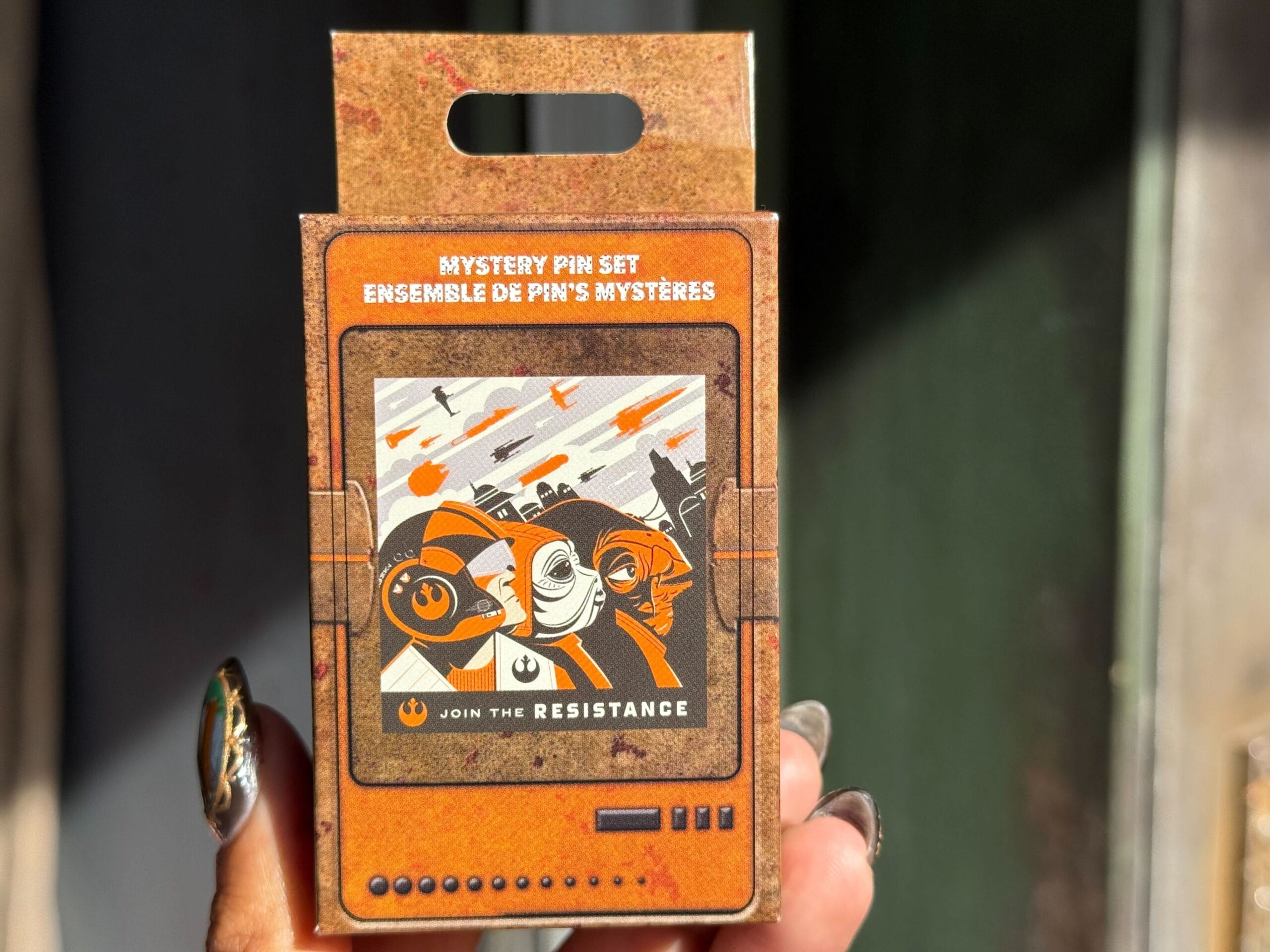 A hand at Disneyland's Galaxy's Edge holds a Star Wars mystery pin set box with Resistance characters and ships on the cover.