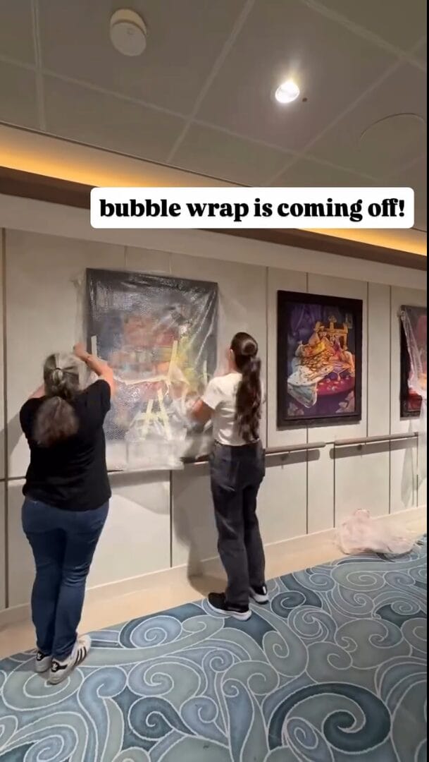 Two people unwrap Disney Imagineering-inspired artwork from bubble wrap on a wall, reminiscent of the magic in Disney parks.
