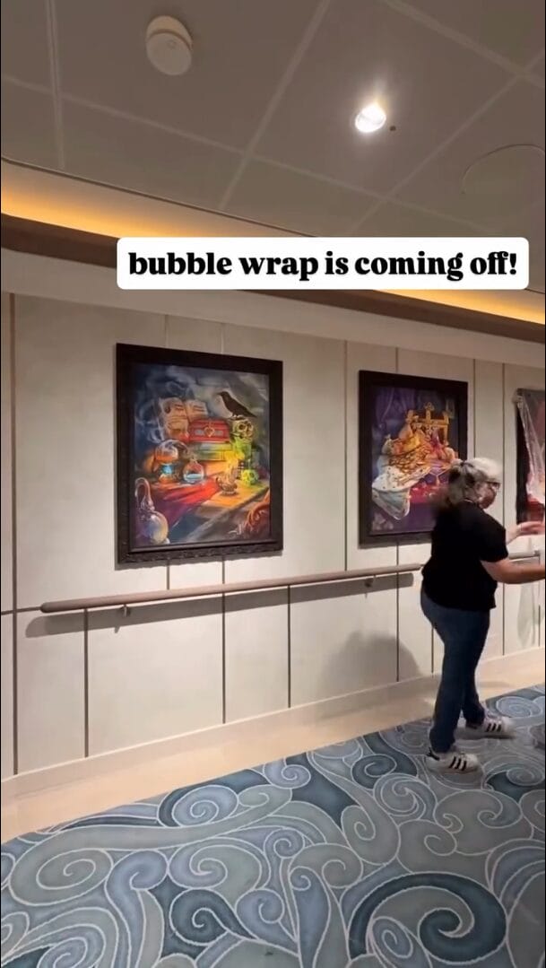 A woman unwraps Disney art in a hallway, next to a sign reading "bubble wrap is coming off!"—no castle like at Disneyland Paris.