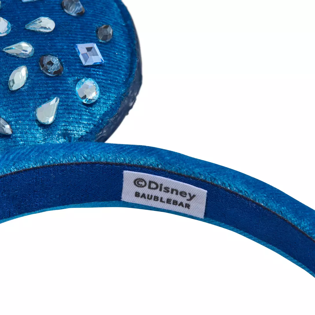 Close-up of a jeweled blue Disney headband, "Disney BaubleBar" label inside, found in Disney Parks merchandise shops worldwide.