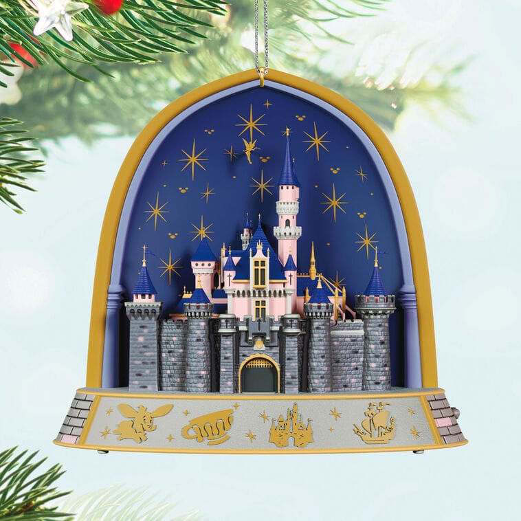 A Disney Keepsake Ornament of a castle, resembling Cinderella Castle from Walt Disney World, hangs on a tree with stars and zodiac symbols at its base.