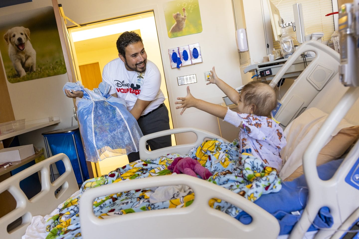 A smiling man donates a Disney Halloween dress to an excited hospitalized child.