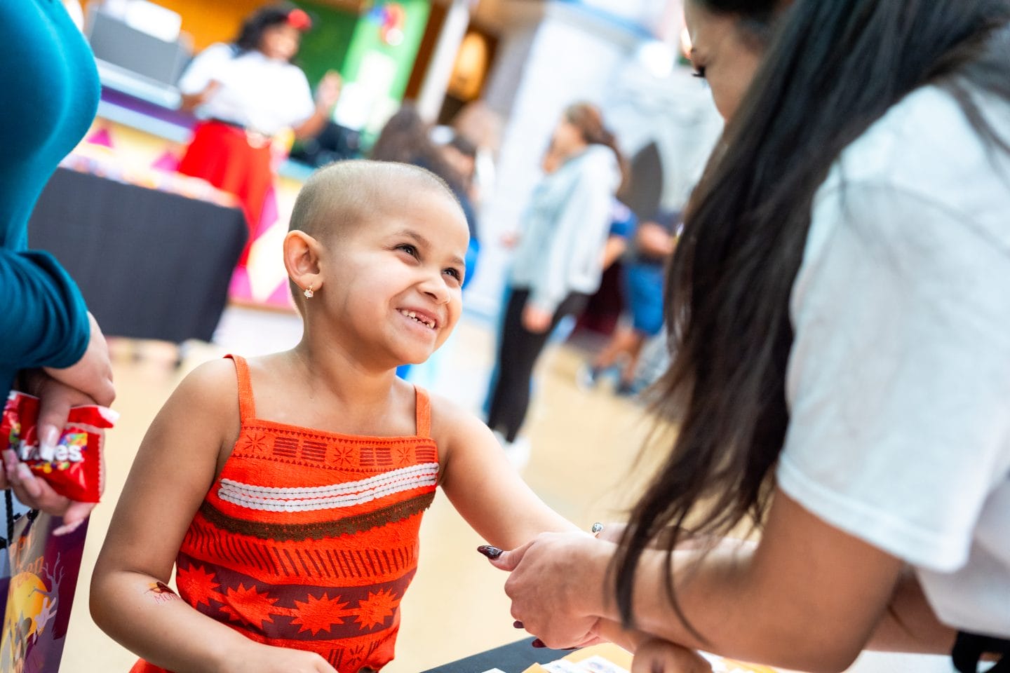 A smiling young girl in a red dress gets her hand painted at a festive Disney park Halloween event, surrounded by cheerful decor.