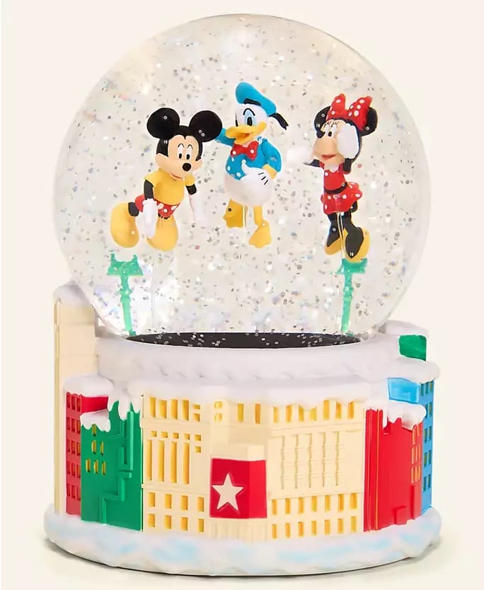 Disney snow globe with Mickey, Donald, and Minnie inside, base featuring Macy’s holiday buildings; no castle like iconic park castles.