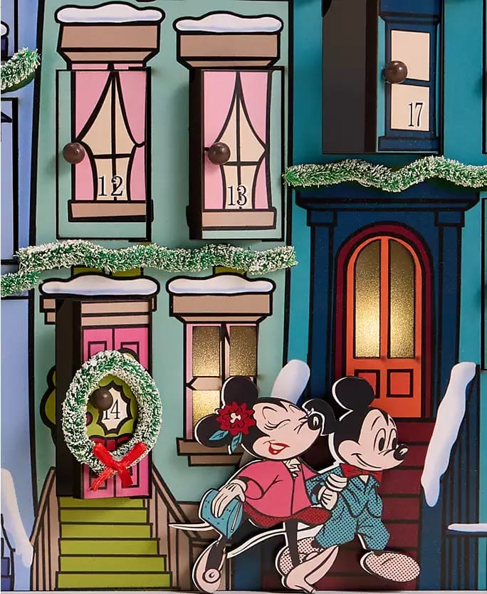 Minnie and Mickey Mouse in pajamas walk by snowy townhouses at a Disney Park, part of the 2025 Holiday Collection. No castle visible.