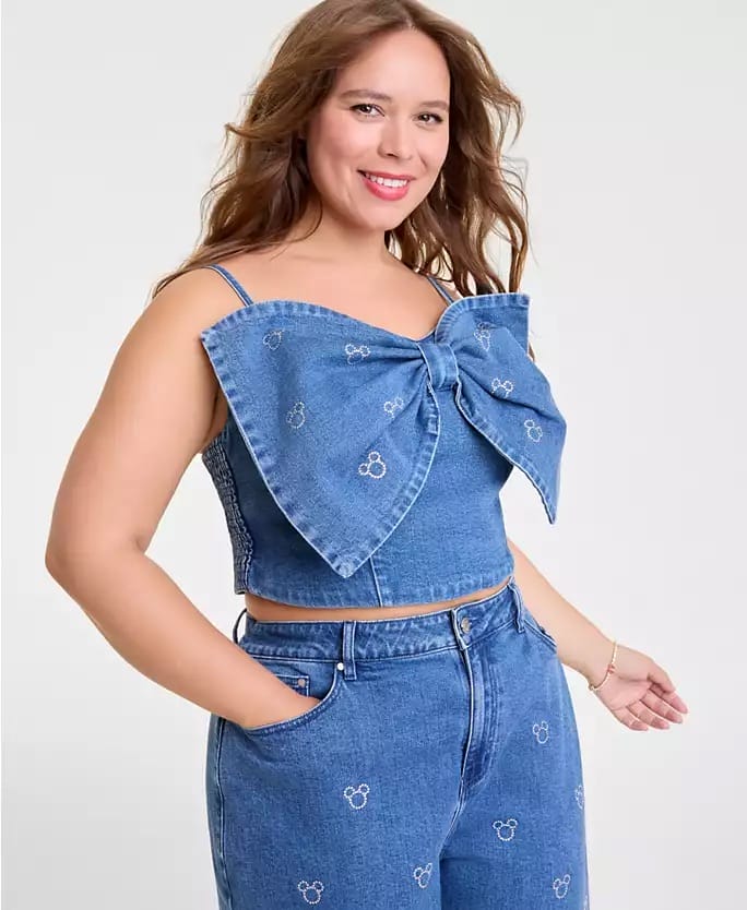 Smiling woman in Disney 2025 Holiday Collection denim crop top and Mickey jeans, reminiscent of park fashion seen near castle views.
