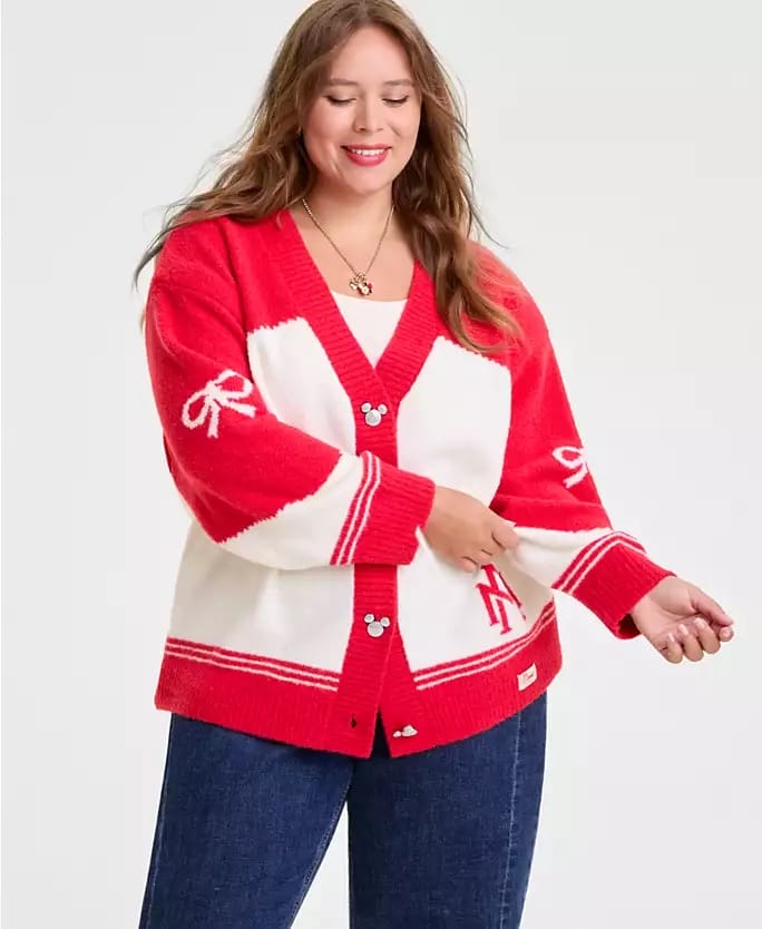 Smiling woman at a Disney park in a red and white Disney Holiday cardigan with bow details, Mickey Mouse buttons, and blue jeans.