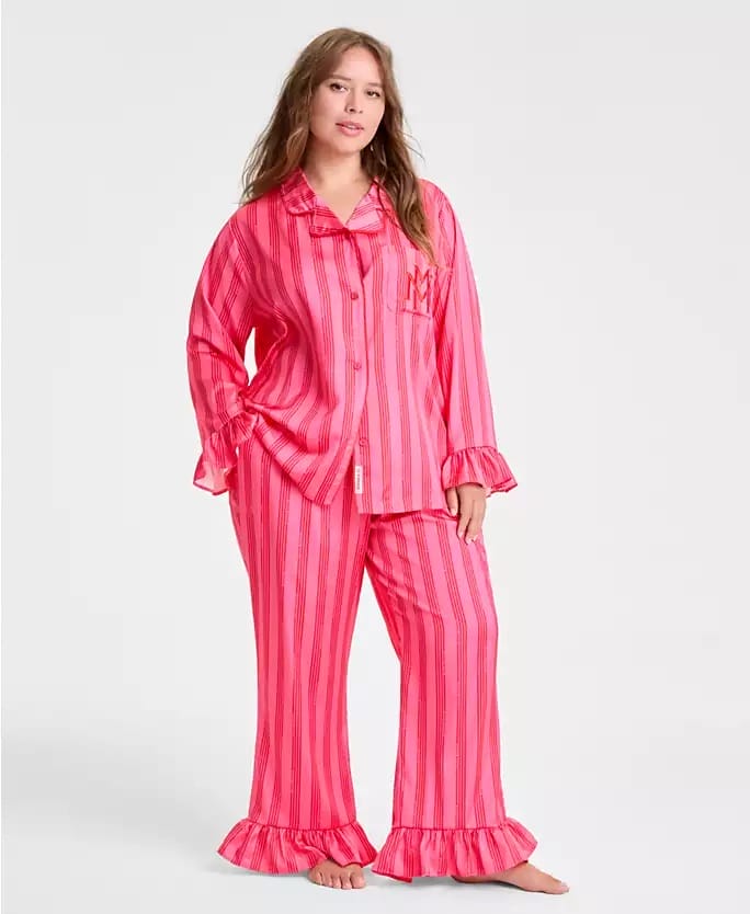 Woman in pink striped Macy’s Holiday pajamas, barefoot, stands on plain backdrop—no Sleeping Beauty or Cinderella Castle present.