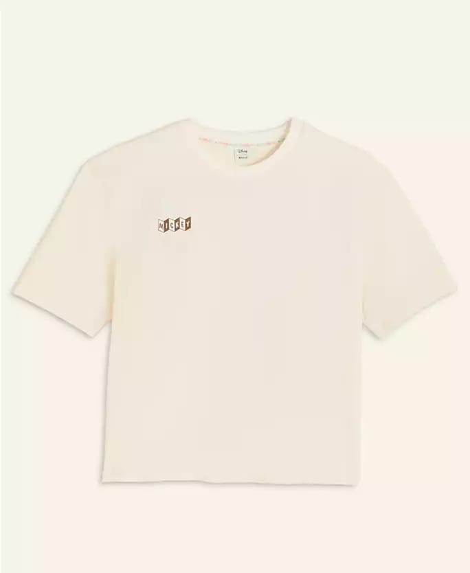 Off-white short-sleeve T-shirt from the Disney 2025 Holiday Collection, featuring a small graphic logo inspired by Disney Parks.