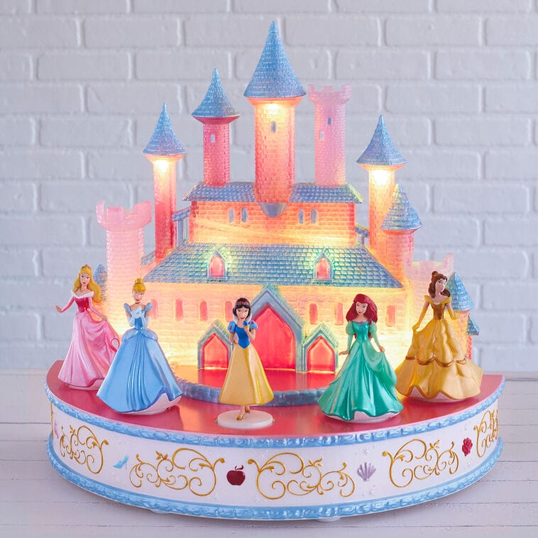 Five princess figurines stand before a glowing castle resembling Disney's Cinderella Castle, part of Hallmark Keepsake Ornaments.