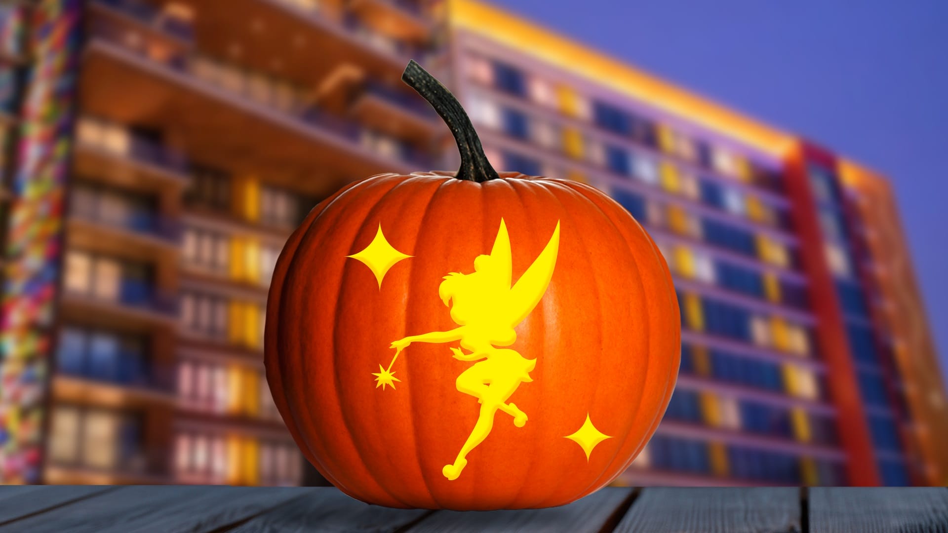 A pumpkin with Disney fairy and star carvings glows, with a modern building in the background, not resembling any Disney castle.