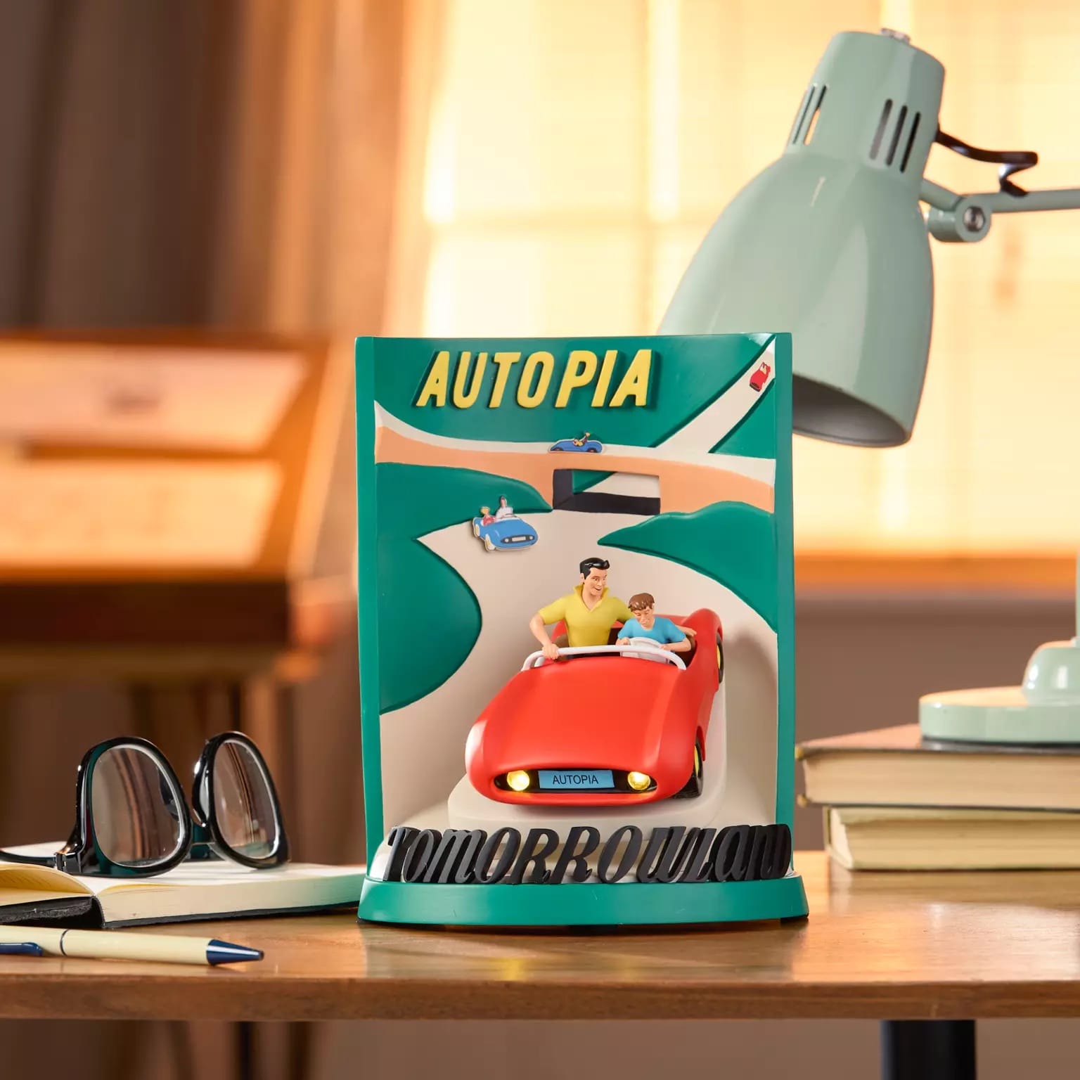 A decorative Autopia Tomorrowland sign on a desk, surrounded by Disney park collectibles in a bright, sunlit room—no castle visible.