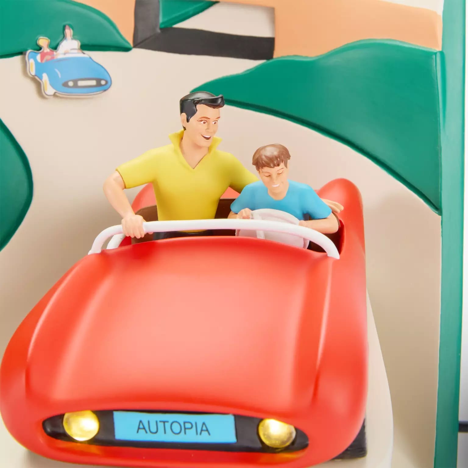 A man and boy smile riding a red Autopia car by a 3D Disney Attraction Poster on a vibrant track, classic Disneyland style.