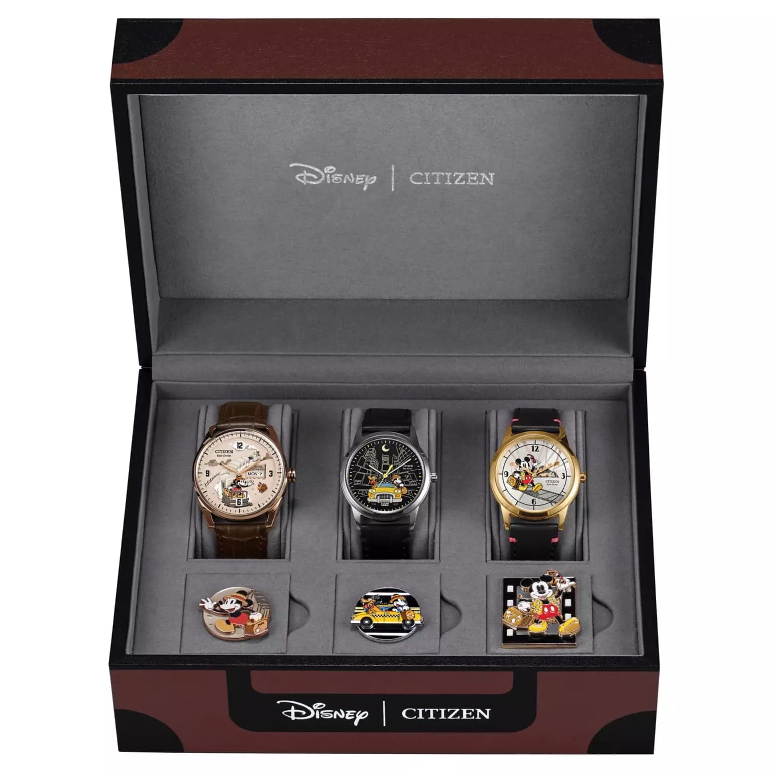 Three Citizen travel watches and three Mickey Mouse Disney pins in a black and brown gift box, reminiscent of park merchandise.
