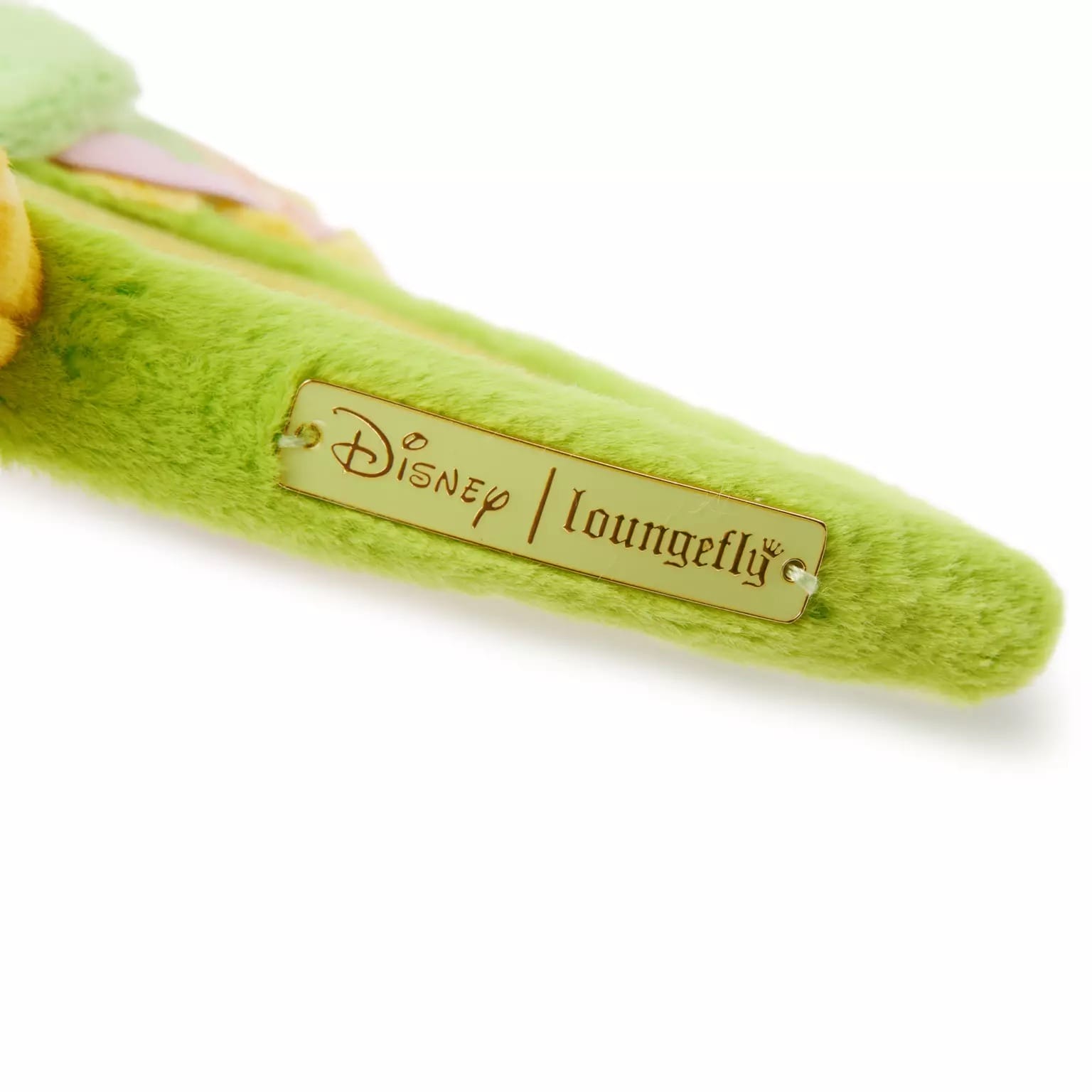 Close-up of a gold Disney Loungefly tag on green plush, part of the Pastel Pascal Ear Headband, found at Disney parks boutiques.