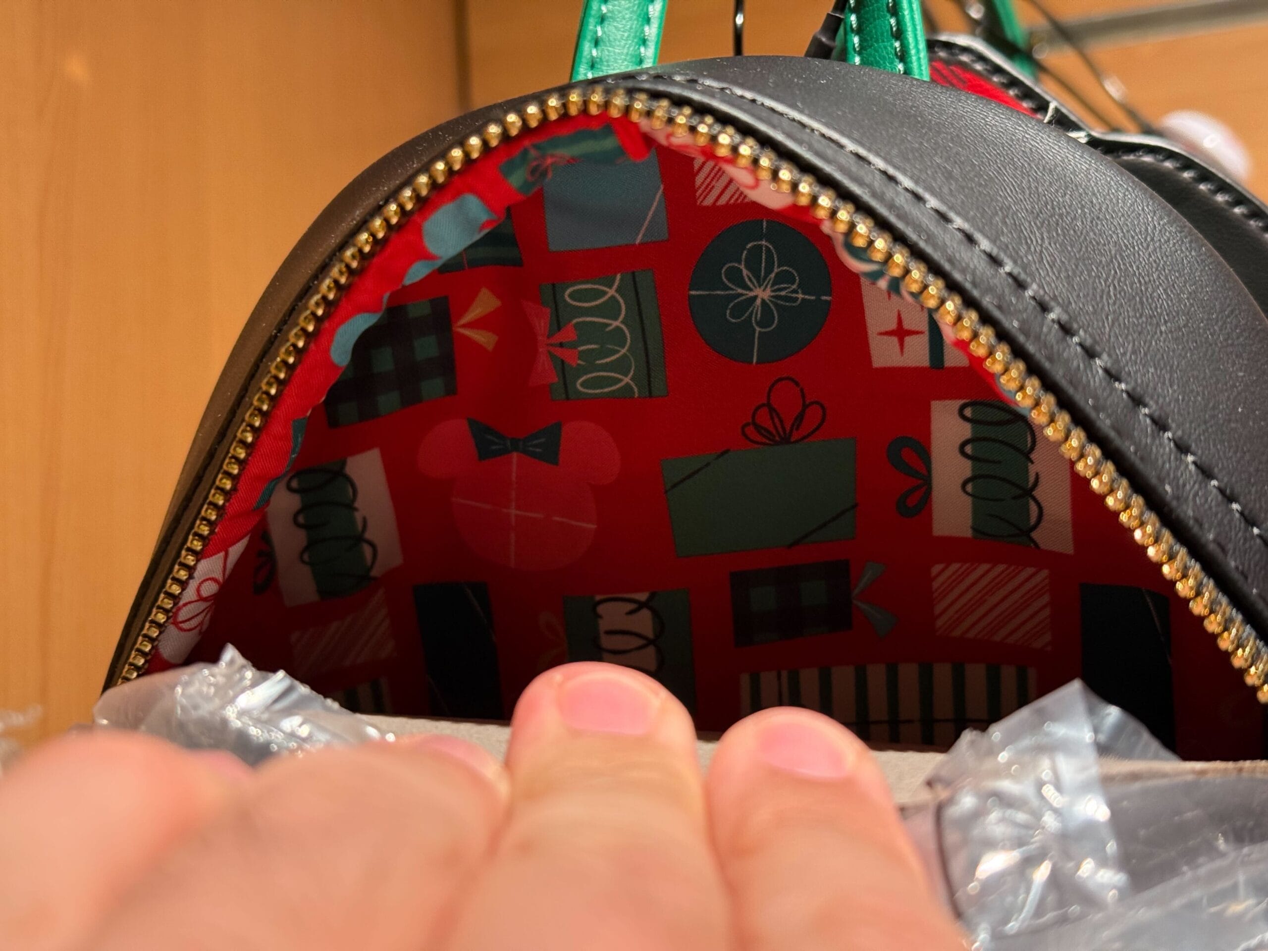 A hand opens a black Christmas Loungefly backpack, revealing a red lining with gift and bow patterns inside.